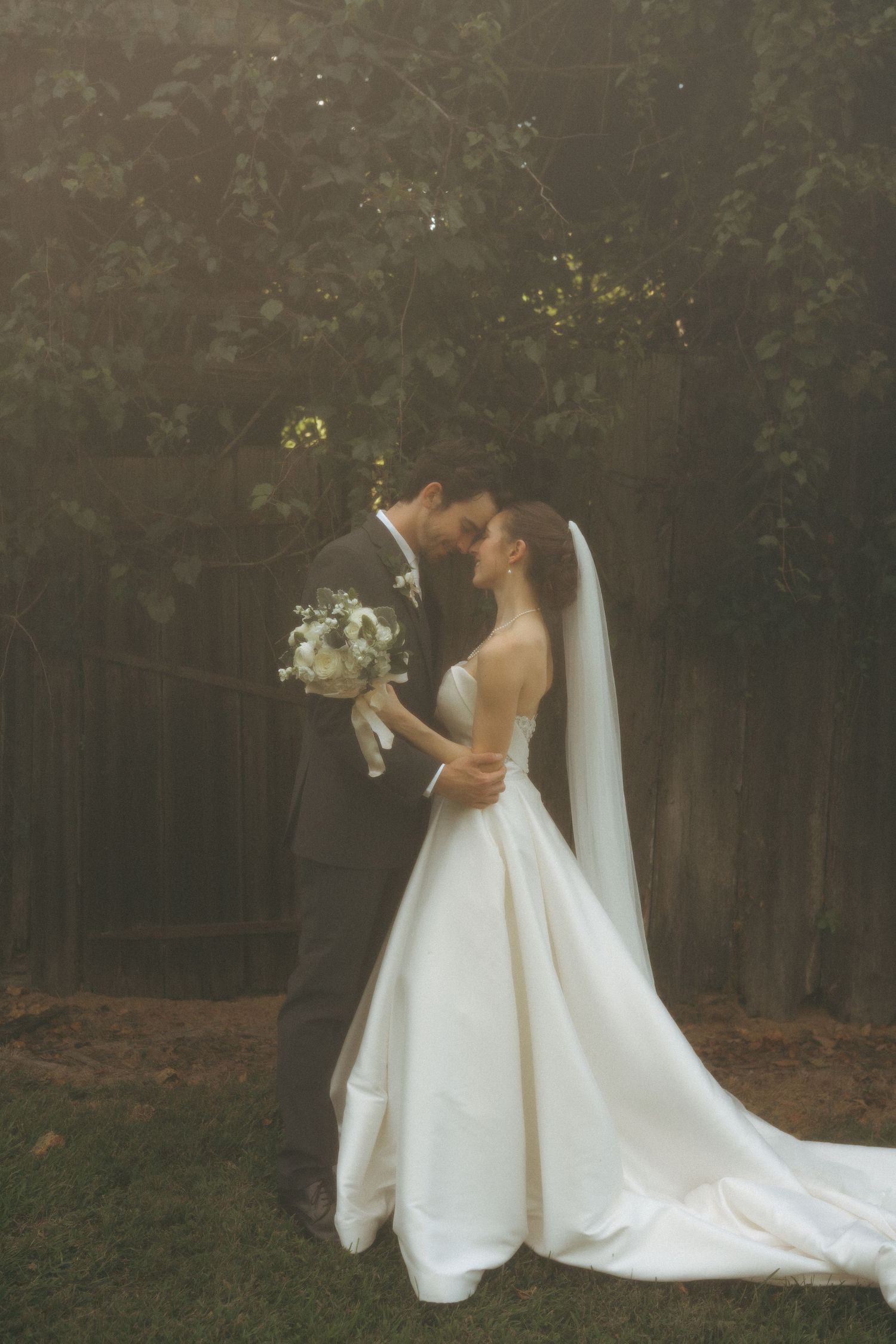 Bride and groom embracing in golden light, bride holding white bouquet in elegant ball gown.