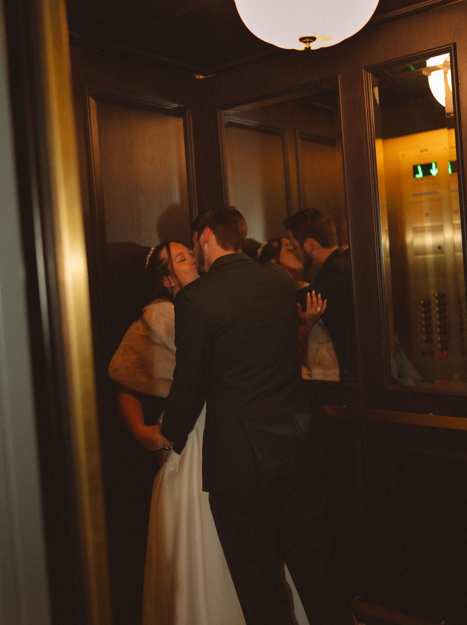 Bride and groom sharing a romantic kiss in a vintage elevator on their wedding day.