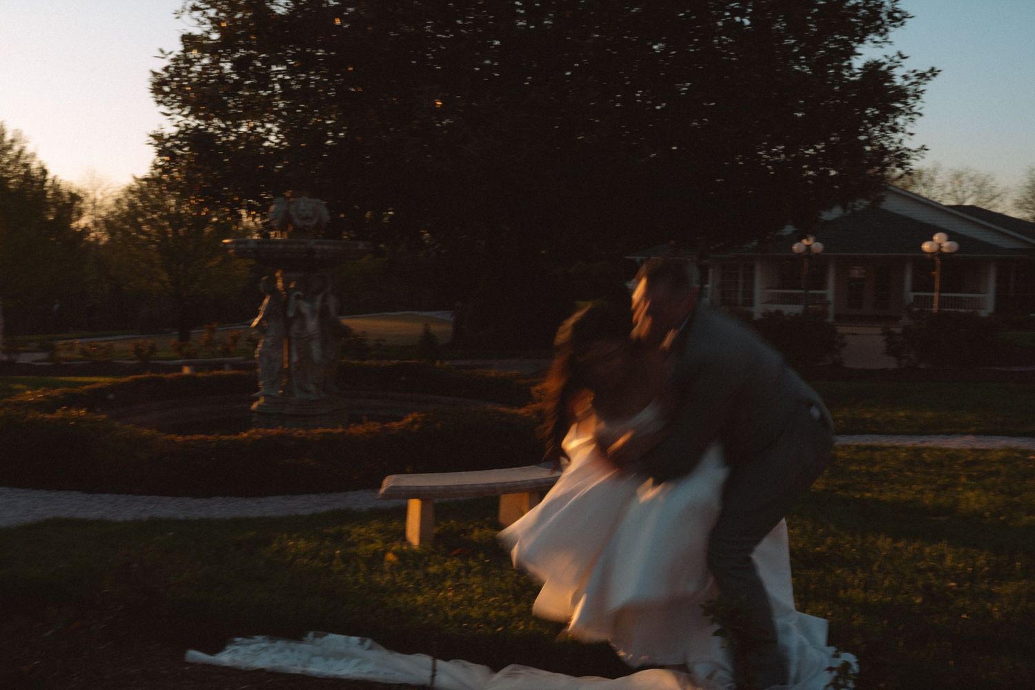 Couple sharing a romantic dance at sunset in a garden, bride in white dress, warm golden light.