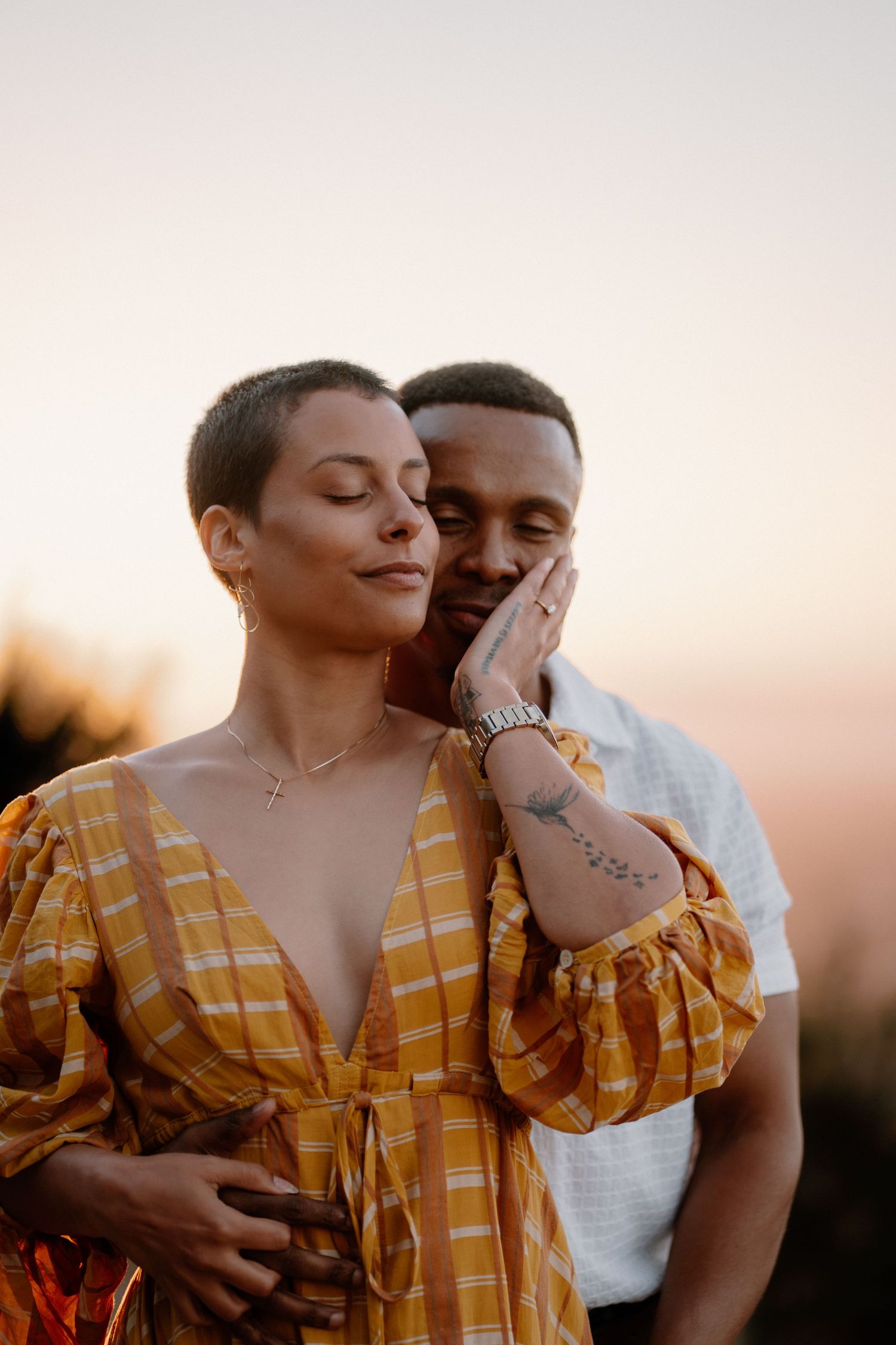 Couple sharing a tender moment at sunset, woman in yellow dress gently touching man's face.