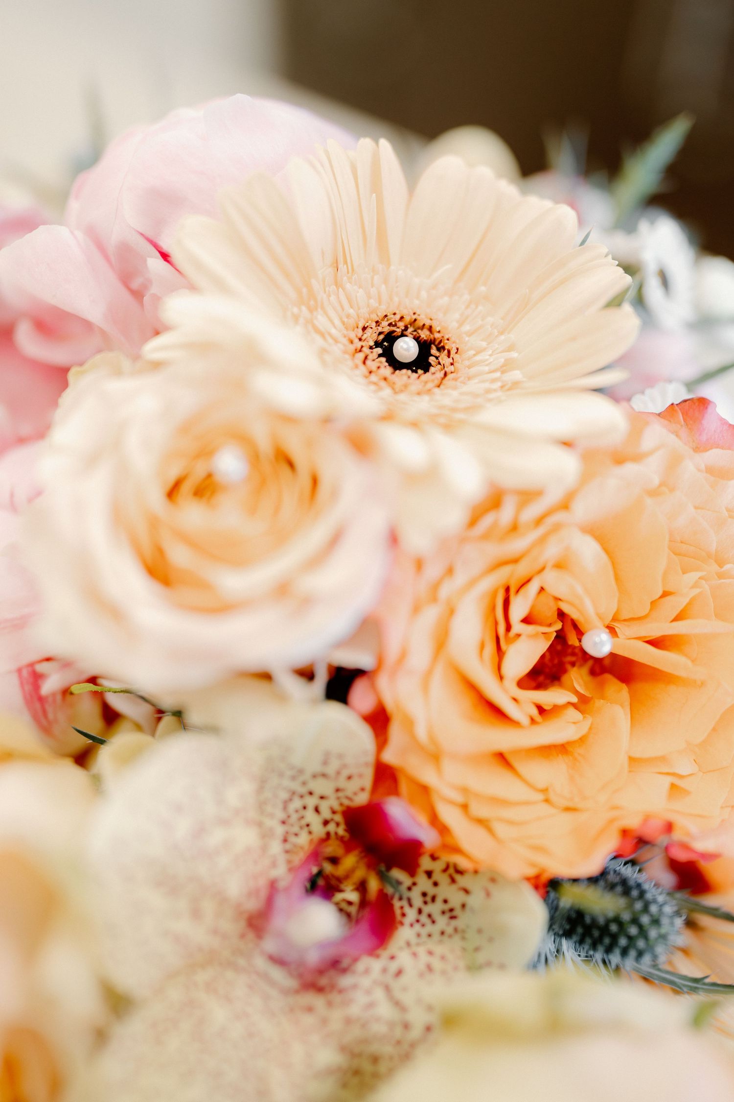 Close-up of a pastel wedding bouquet featuring peach roses, pink gerbera daisy, and delicate mixed blooms.