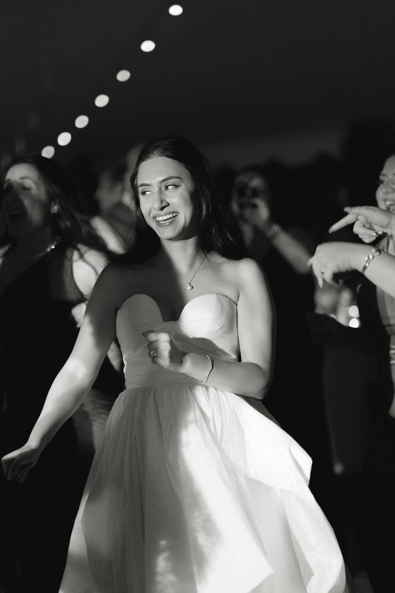 A bride in a strapless white gown dances joyfully at her wedding reception in black and white.