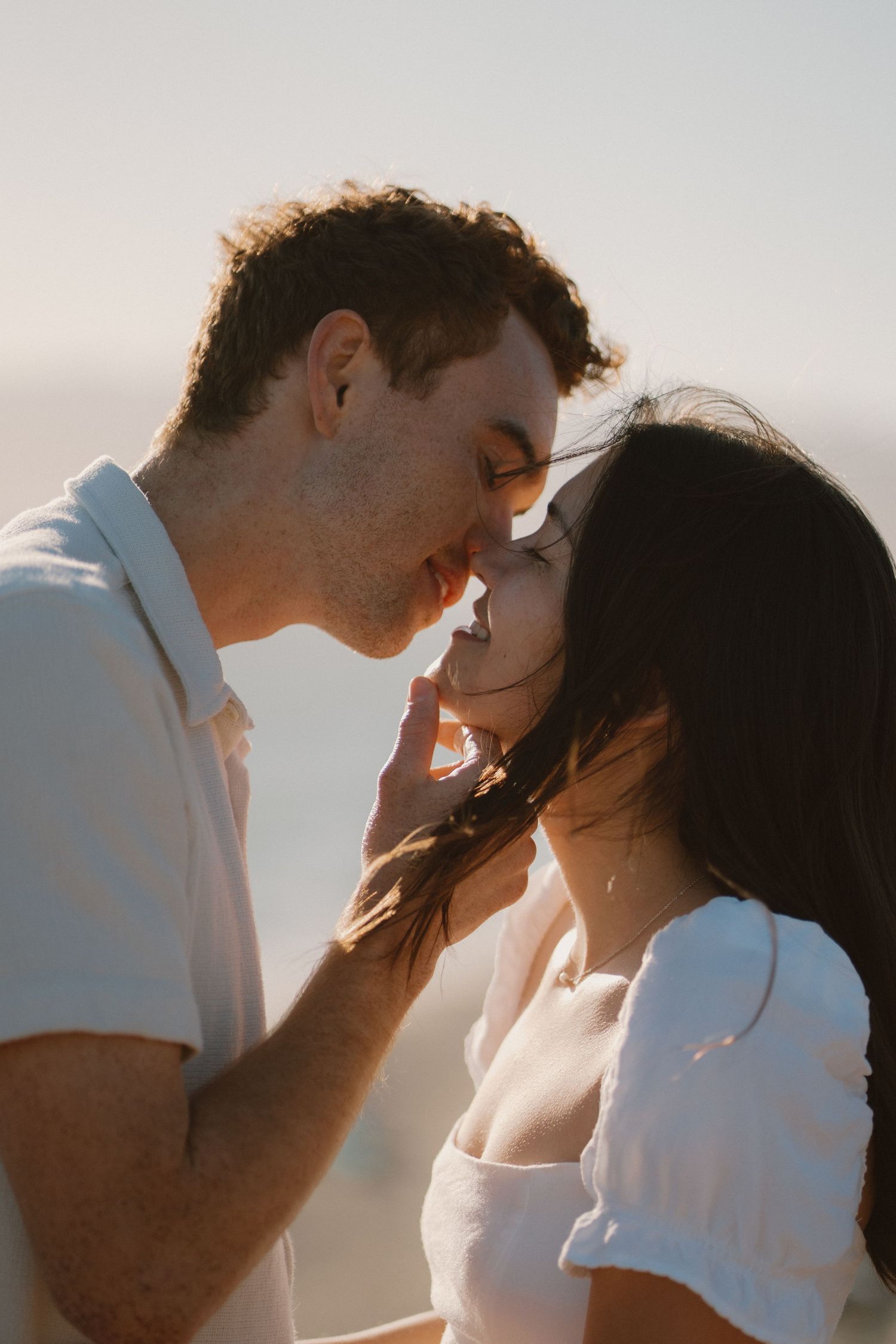 Romantic couple leaning in for a kiss at sunset, man gently touching womans face outdoors.