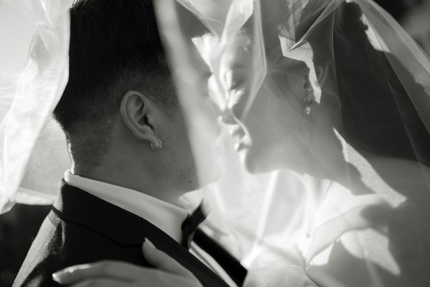 Black and white close-up of bride and groom almost kissing beneath a flowing bridal veil.