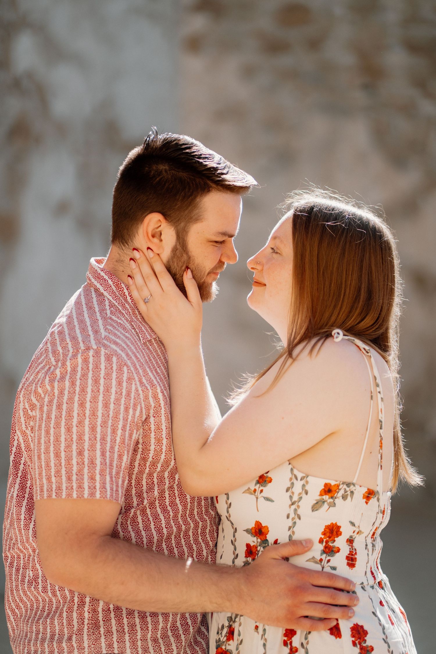 Couple sharing a romantic moment, woman smiling as she holds mans face, golden sunlight glowing behind them.
