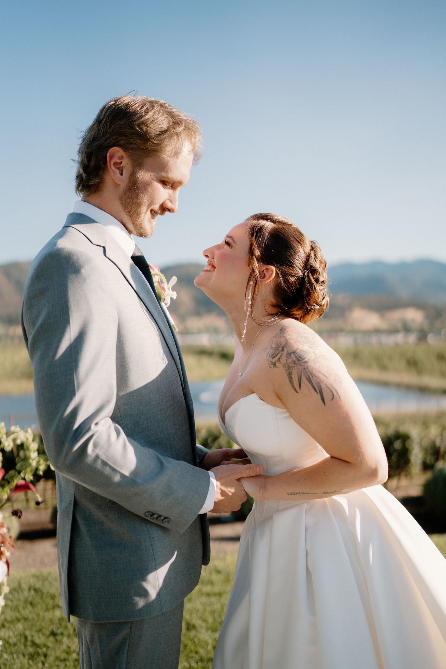 Bride and groom laughing together during outdoor wedding ceremony with mountain backdrop.