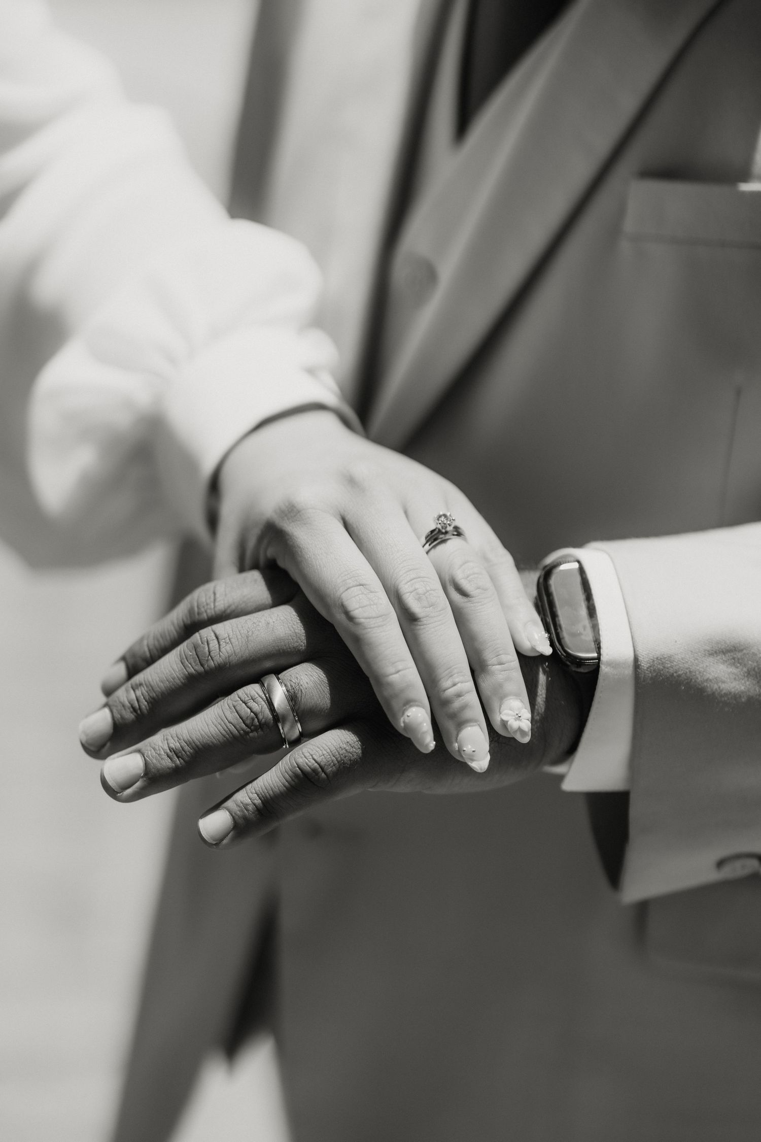 Black and white photo of newlyweds showing off wedding rings, hands together.