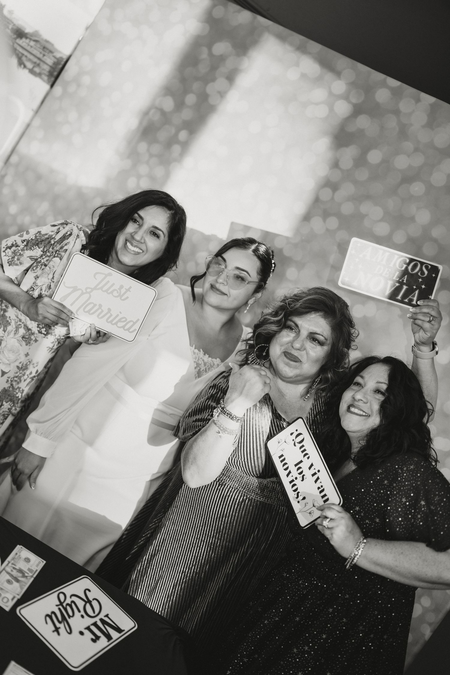 Black and white photo of four women posing with Just Married photo booth props at wedding.