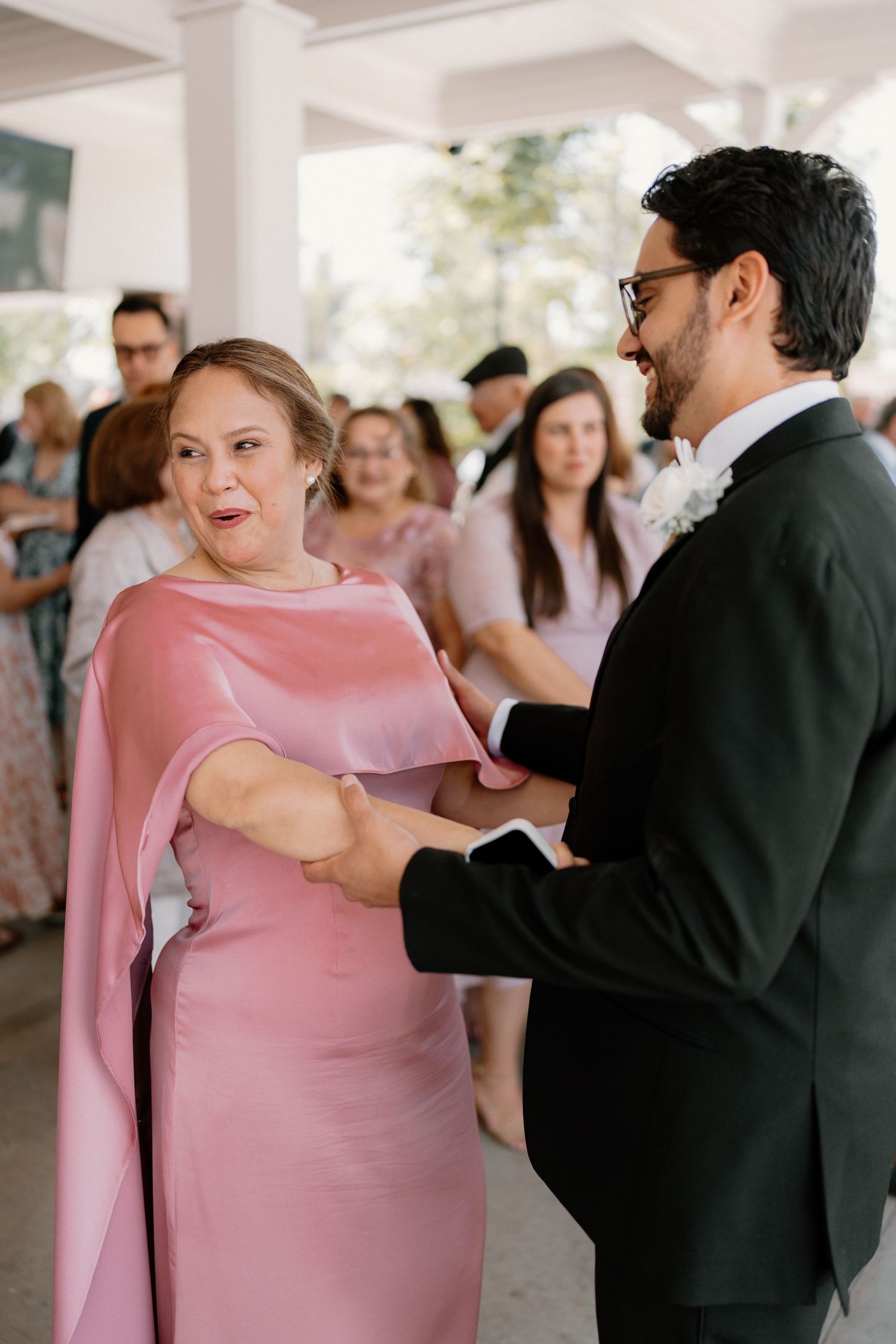 Groom in black suit shares a joyful moment dancing with woman in pink dress at wedding reception.
