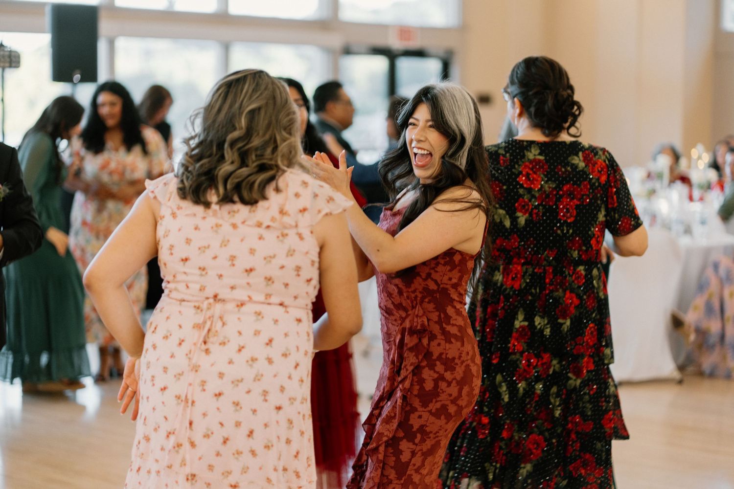 Wedding guests in colorful dresses laugh and dance joyfully together at reception party.