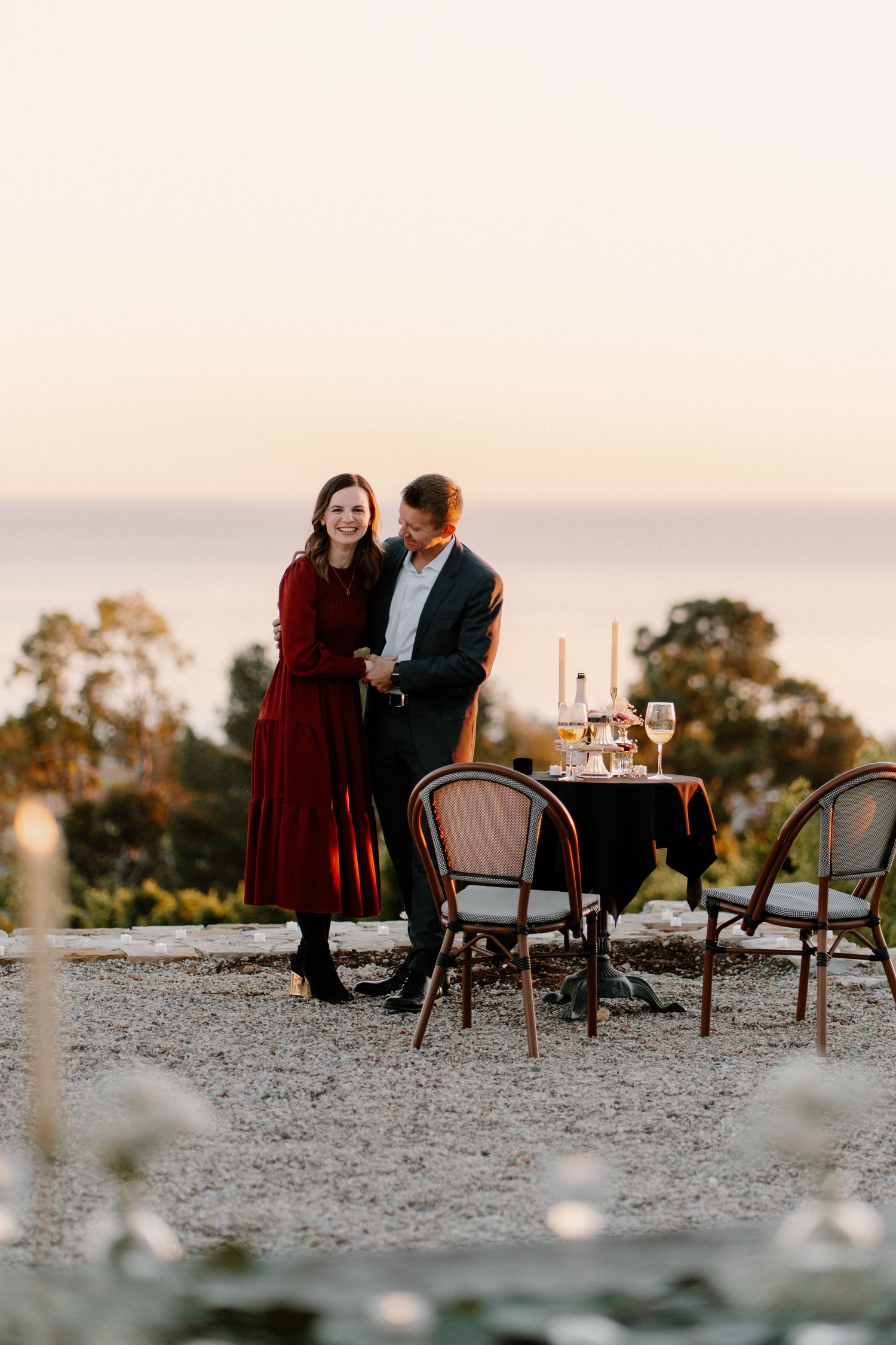 Happy couple holds hands beside a candlelit dinner table with ocean backdrop.