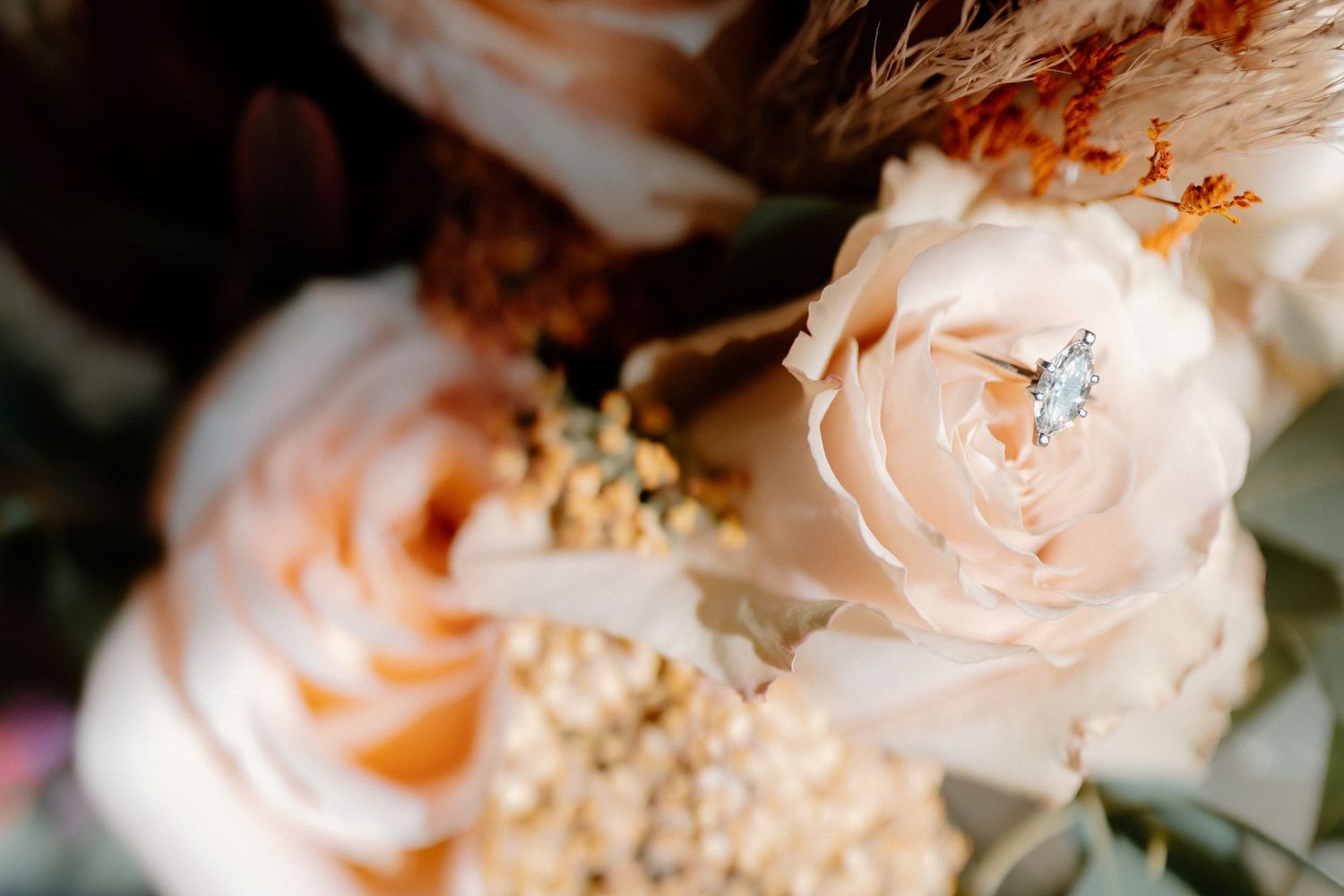 Diamond engagement ring nestled in a blush peach rose within a romantic autumn bridal bouquet close-up.
