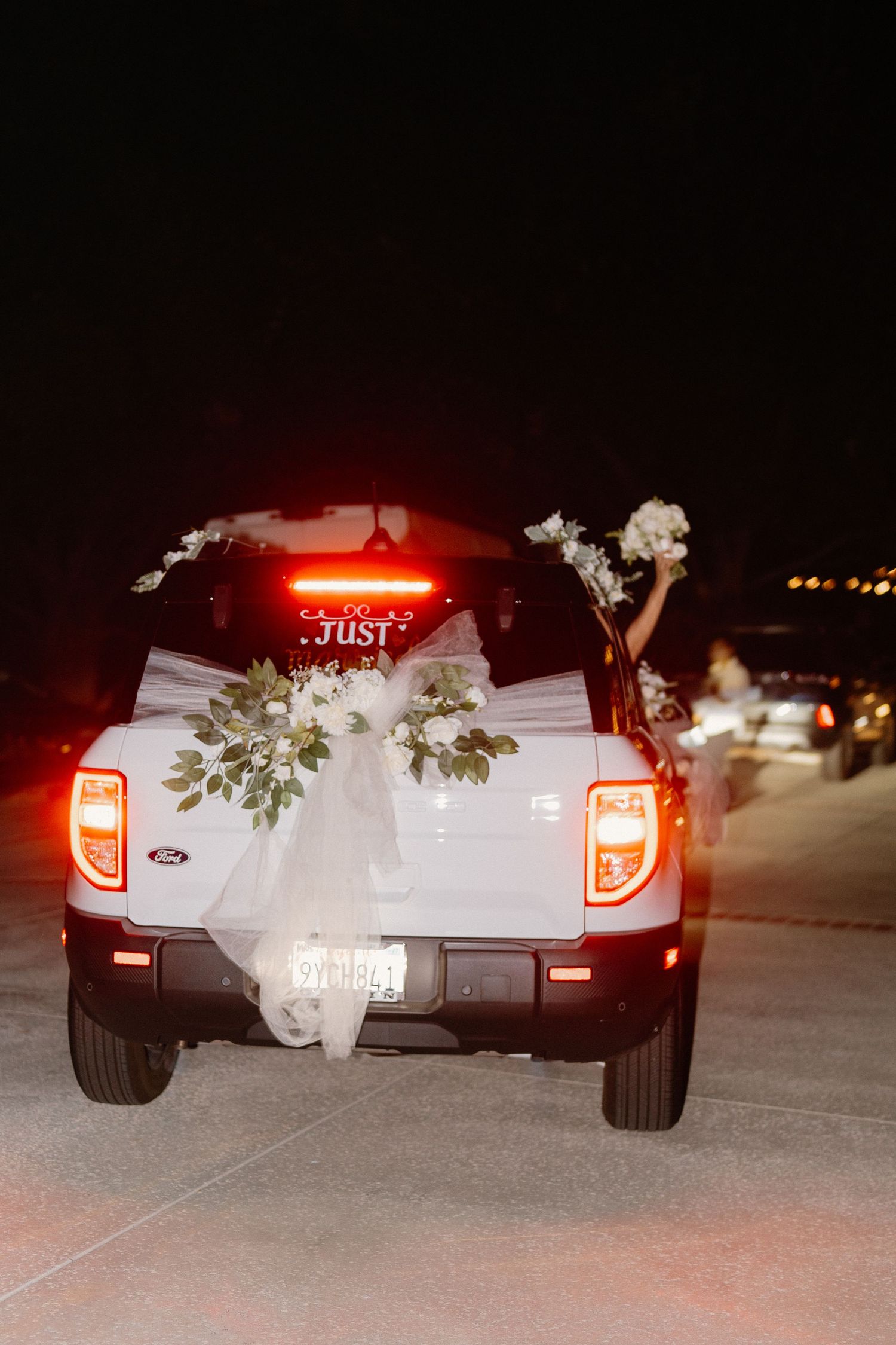 White Ford wedding getaway truck decorated with flowers and ribbons drives away at night.