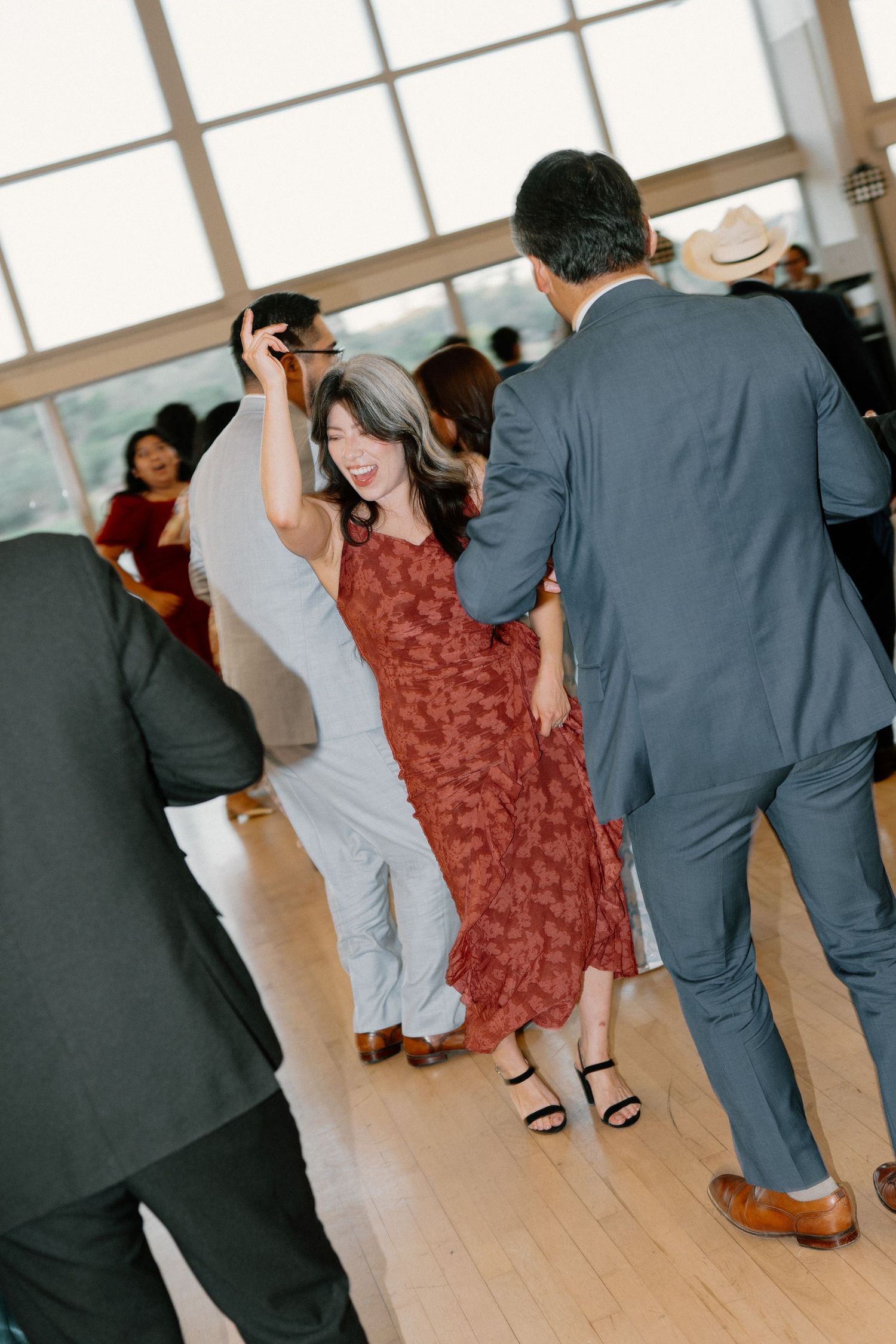 Wedding guest in red floral dress dances and spins on the reception dance floor.