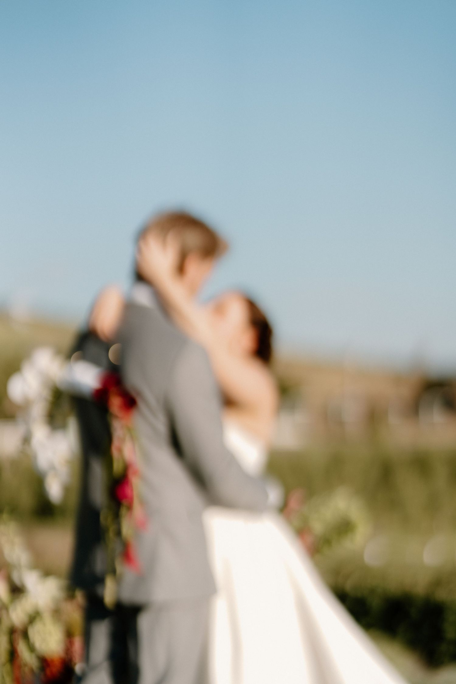 A blurred artistic photo of a bride and groom embracing outdoors under a clear blue sky on their wedding day.