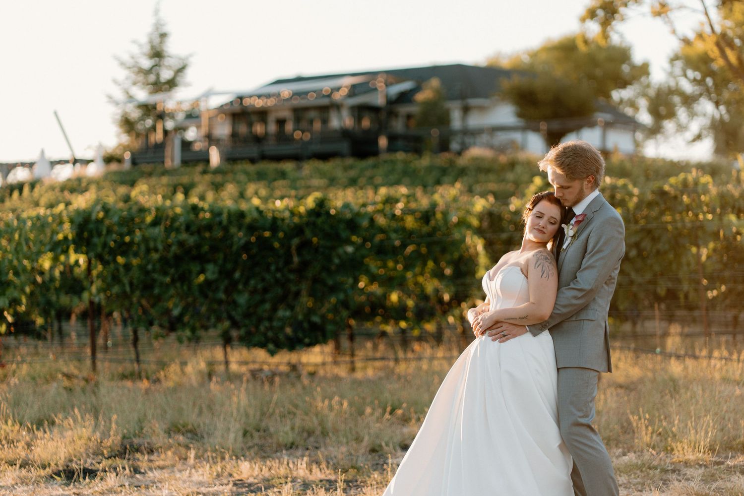 Bride and groom embracing in golden hour light with vineyard and rolling hills behind them.