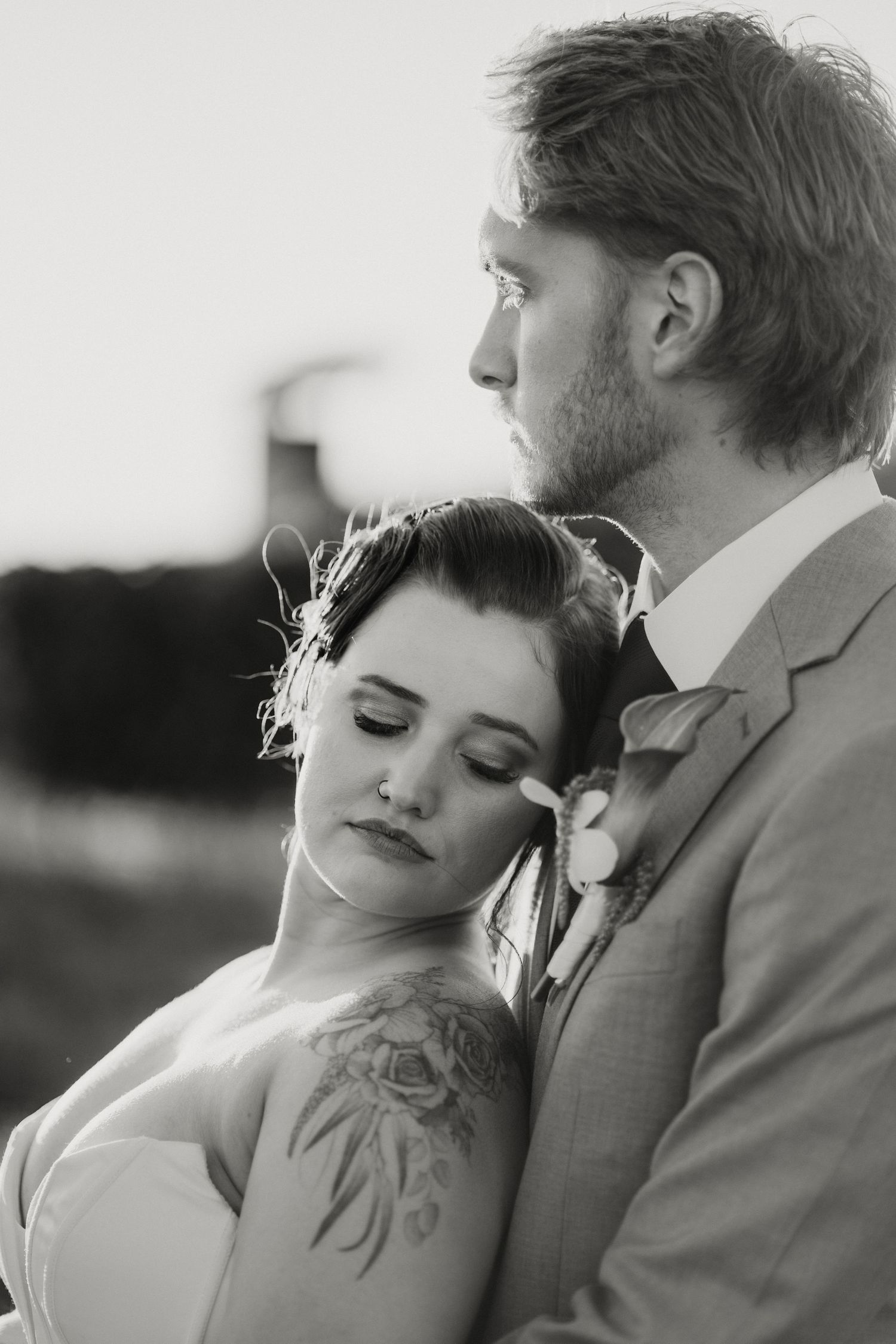 Intimate black and white portrait of bride leaning on groom's chest at their outdoor wedding.