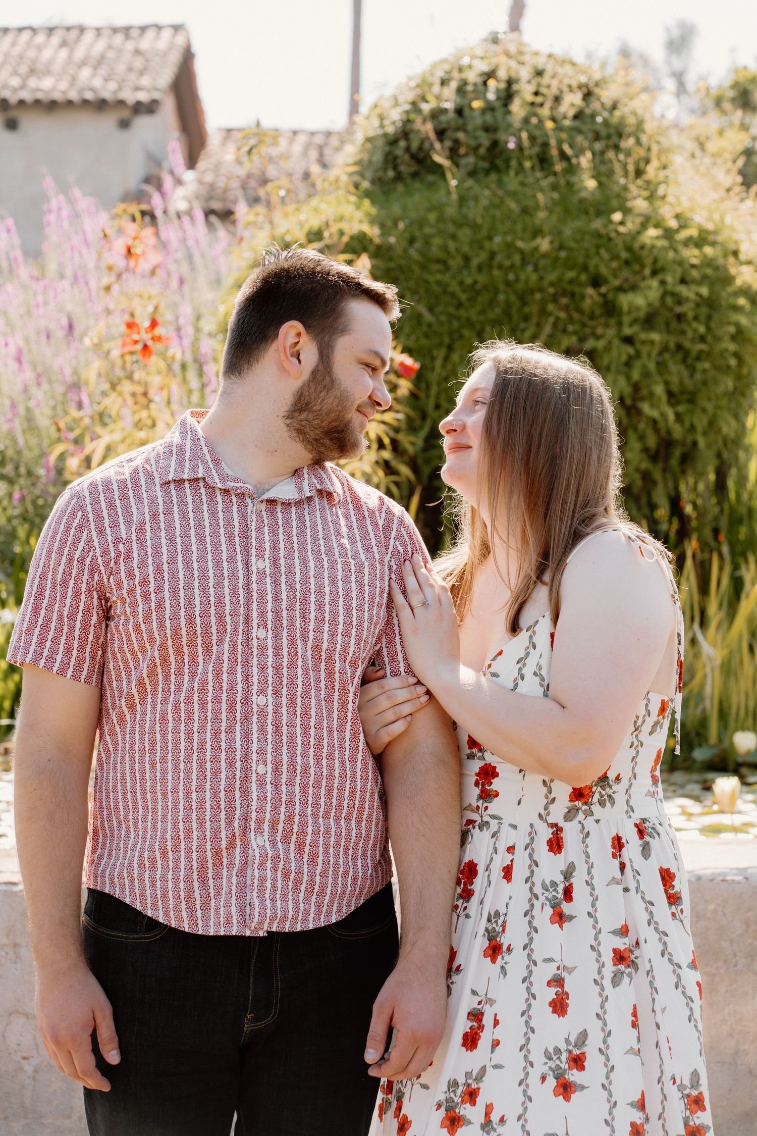 Happy couple laughing together outdoors, woman in floral dress holding mans arm in a garden setting.