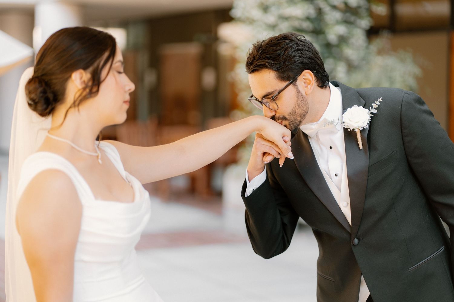 Groom kisses bride's hand tenderly during romantic first look moment at elegant wedding venue.
