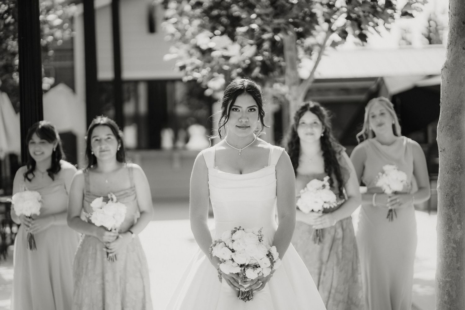 Black and white photo of a bride holding a bouquet with four bridesmaids standing behind her outdoors.