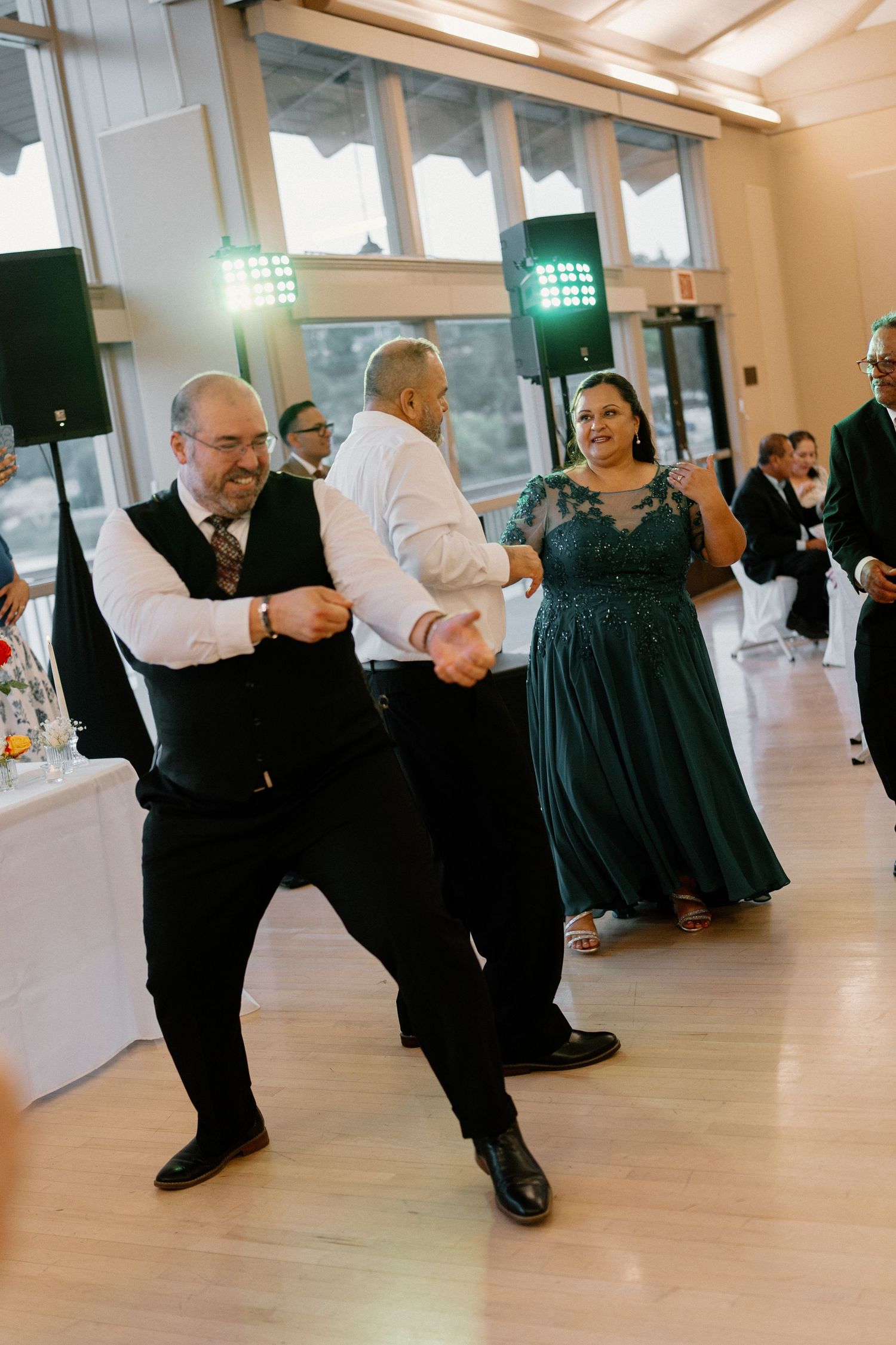 Guests celebrate on the dance floor at a lively wedding reception with colorful lighting.