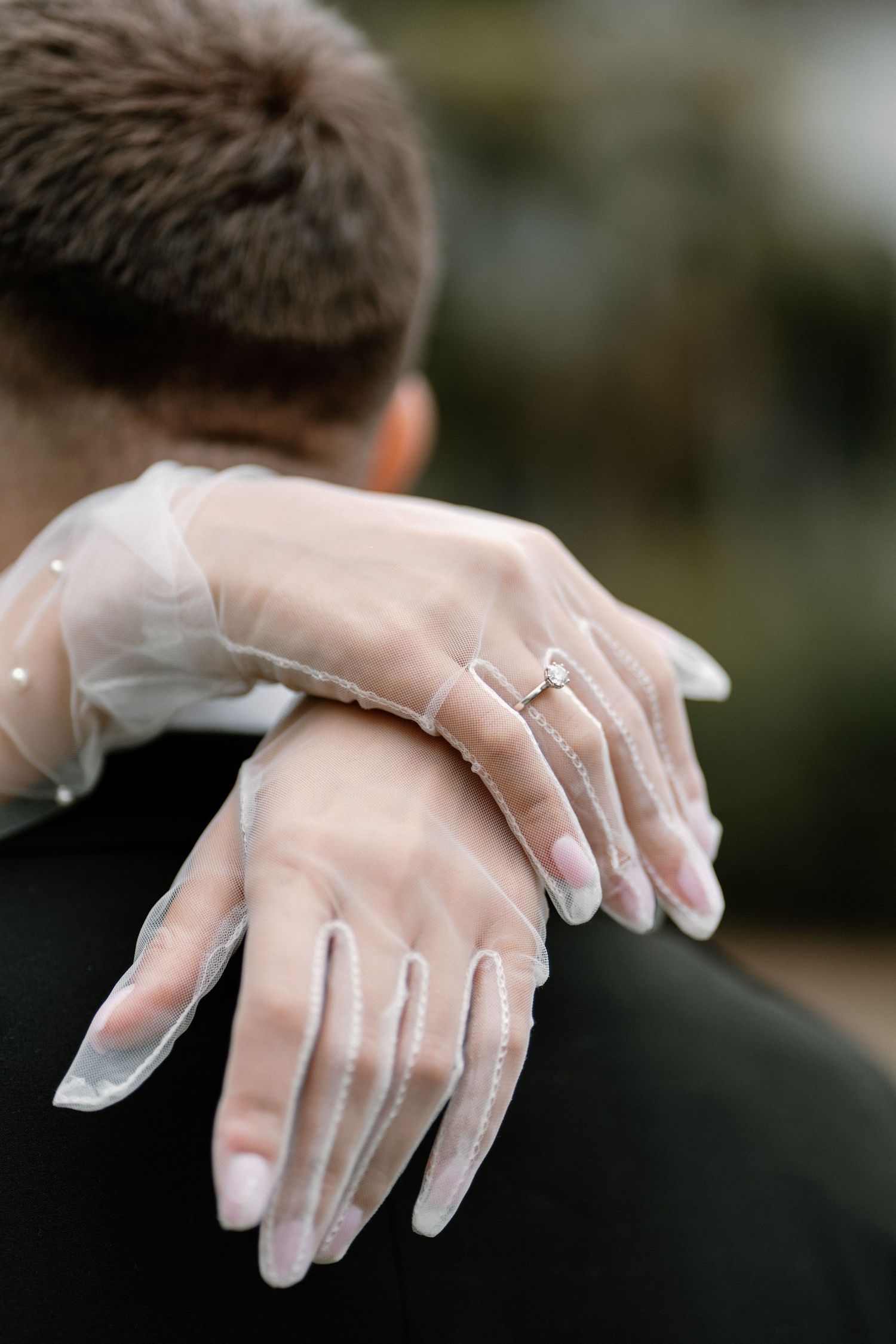 Bride wearing sheer pearl-embellished gloves and diamond ring embracing groom.