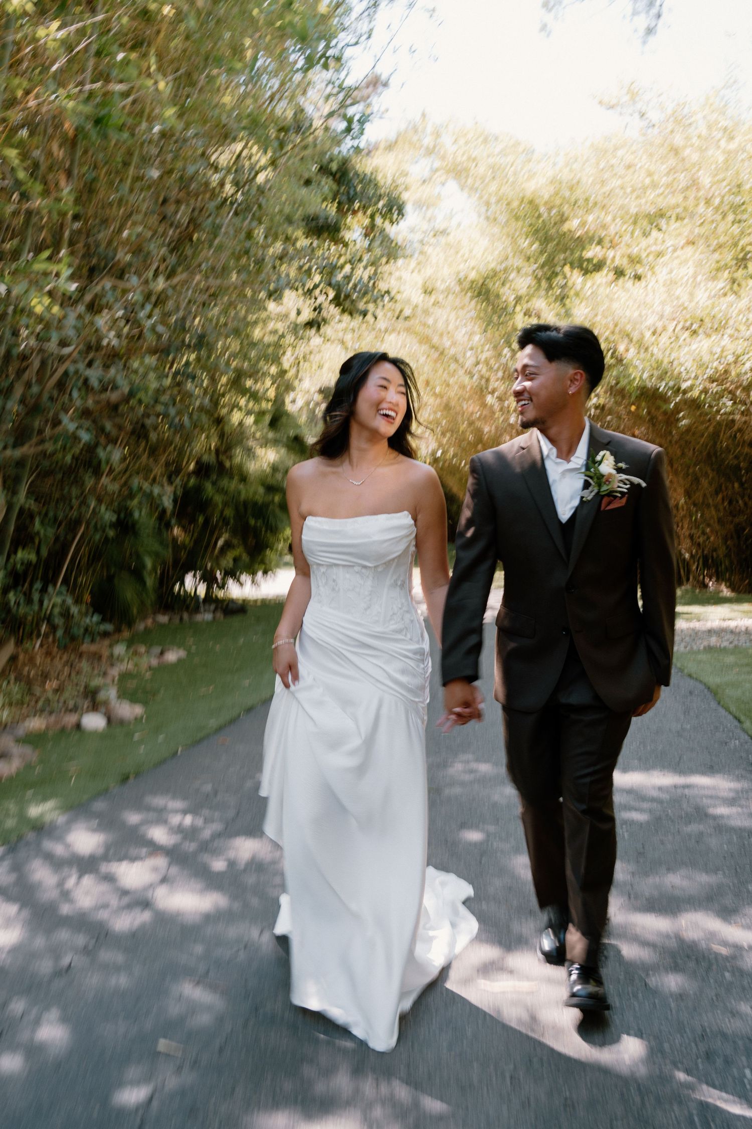 Joyful bride and groom holding hands walking through lush bamboo garden path on wedding day.