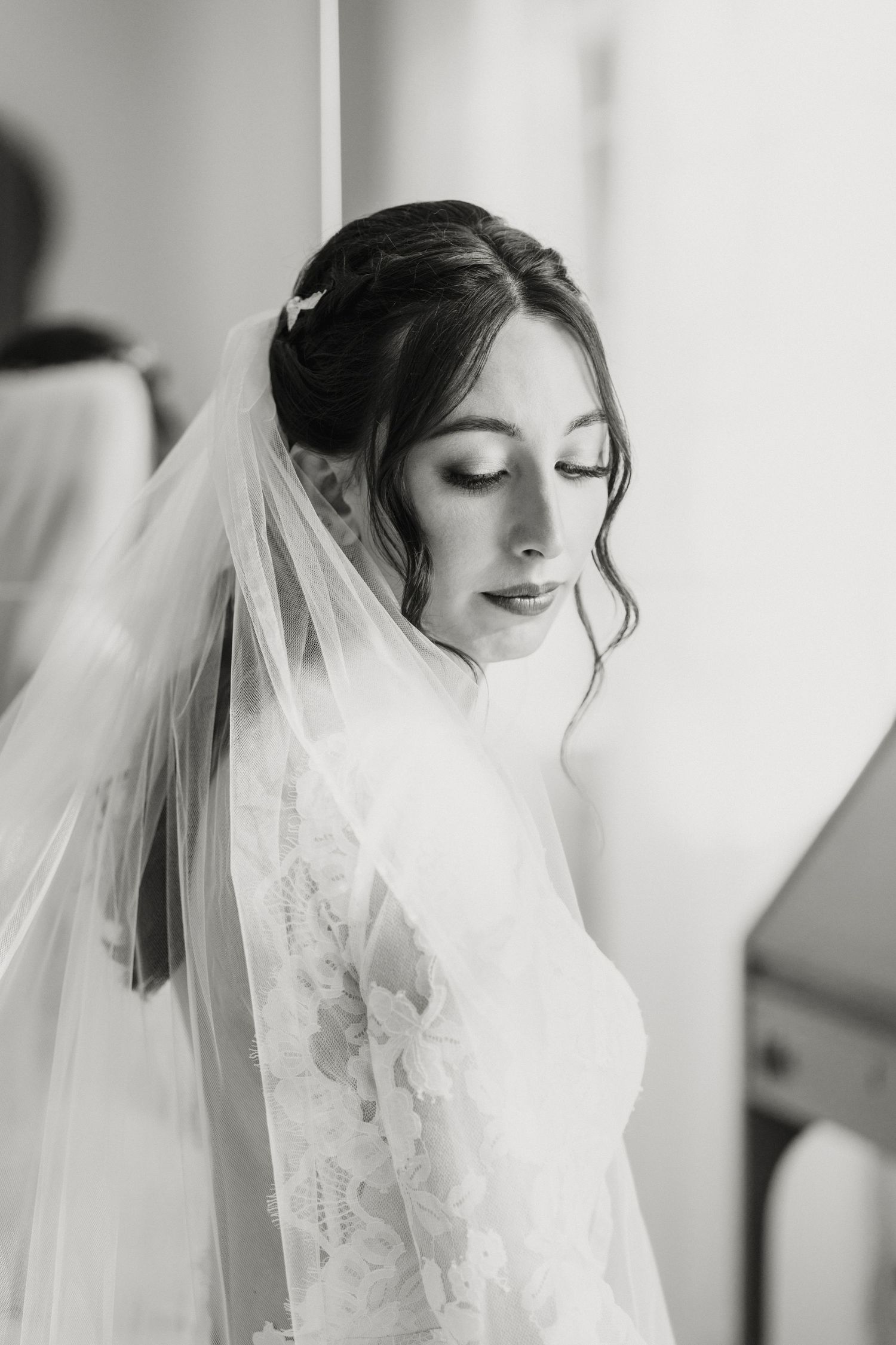 Black and white portrait of a bride in a lace gown and veil looking down gracefully.