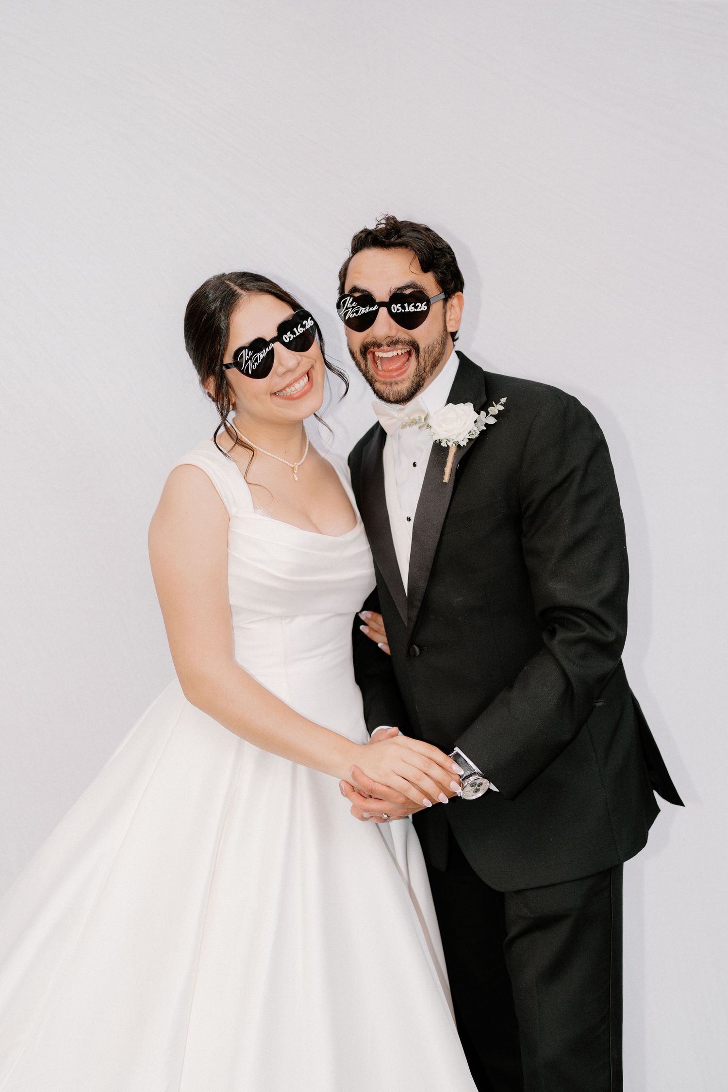 Smiling bride and groom wearing matching black sunglasses with wedding date at photo booth.