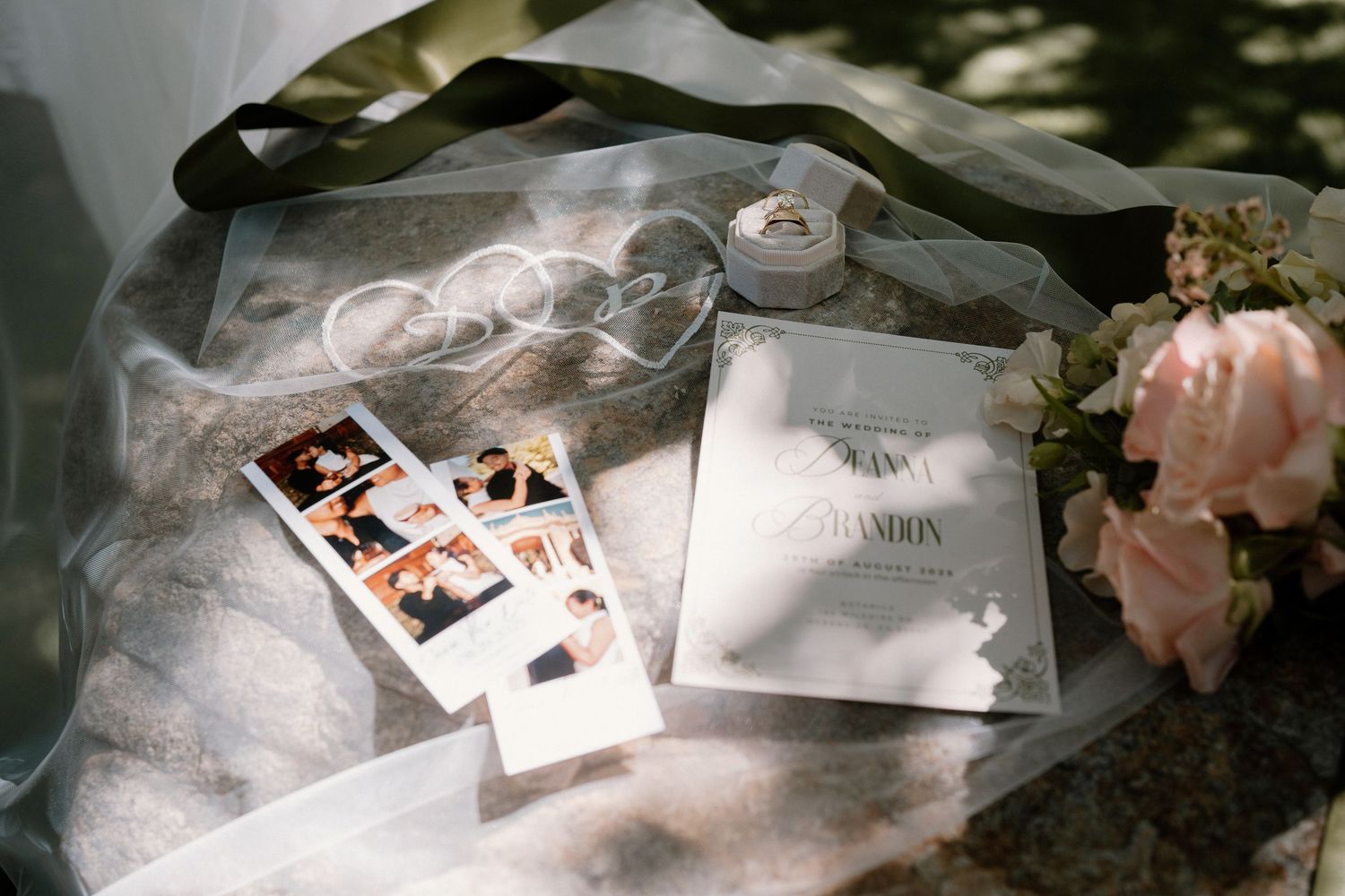 Wedding flat lay with invitation suite, polaroid photos, ring box, and floral details on sheer veil.