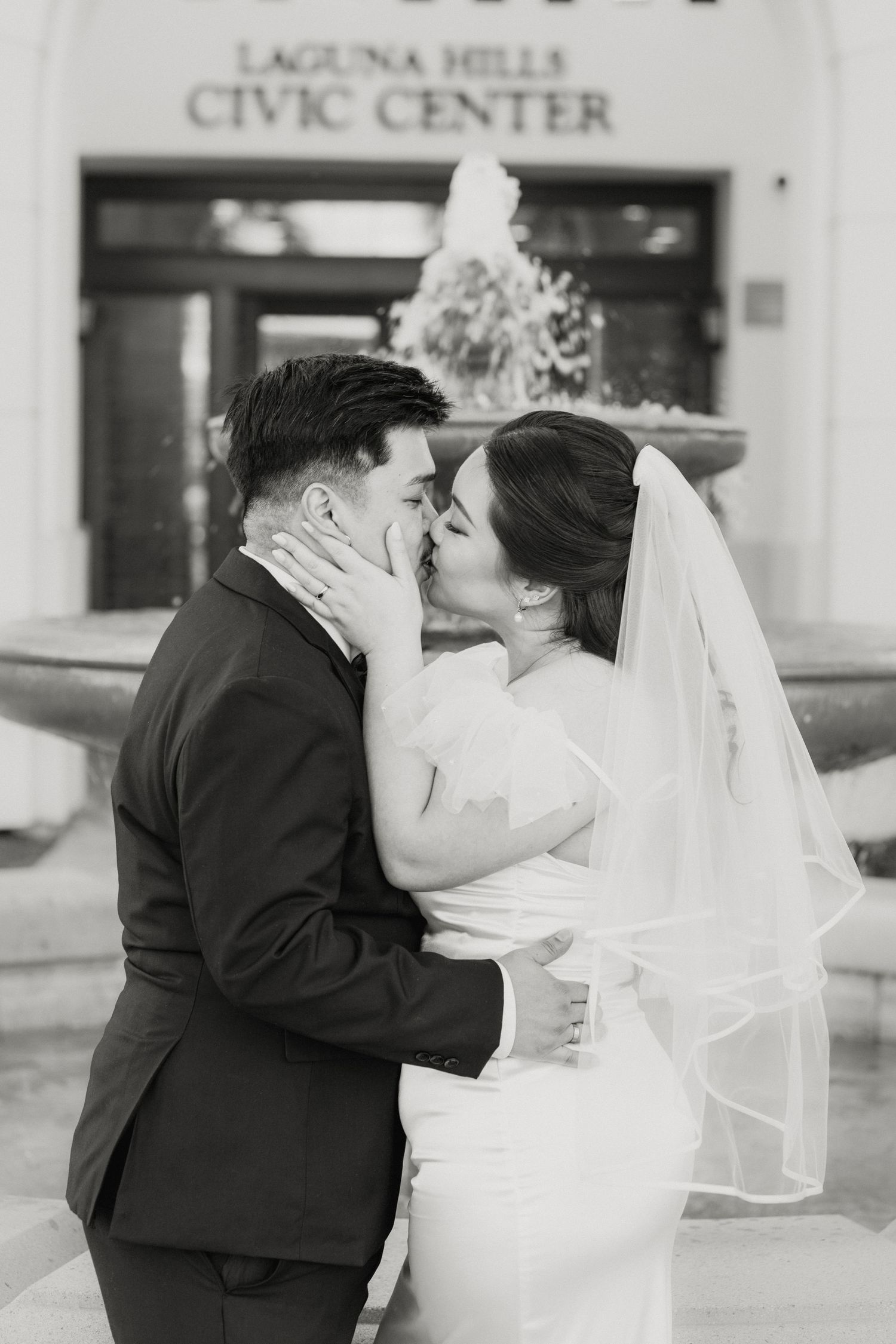 Black and white photo of bride and groom kissing in front of Laguna Hills Civic Center fountain.