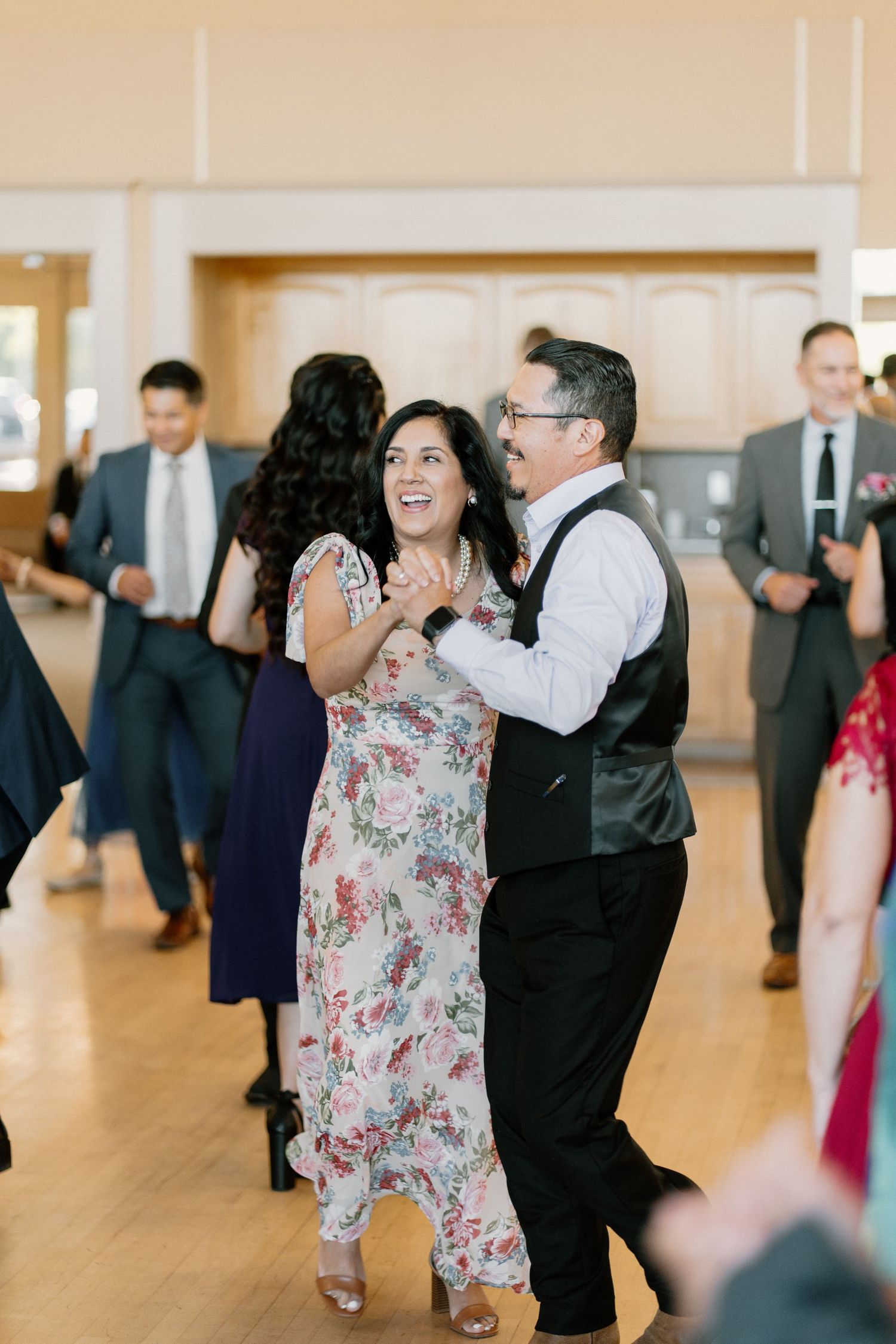 Couple dancing joyfully at wedding reception in bright ballroom with other guests.