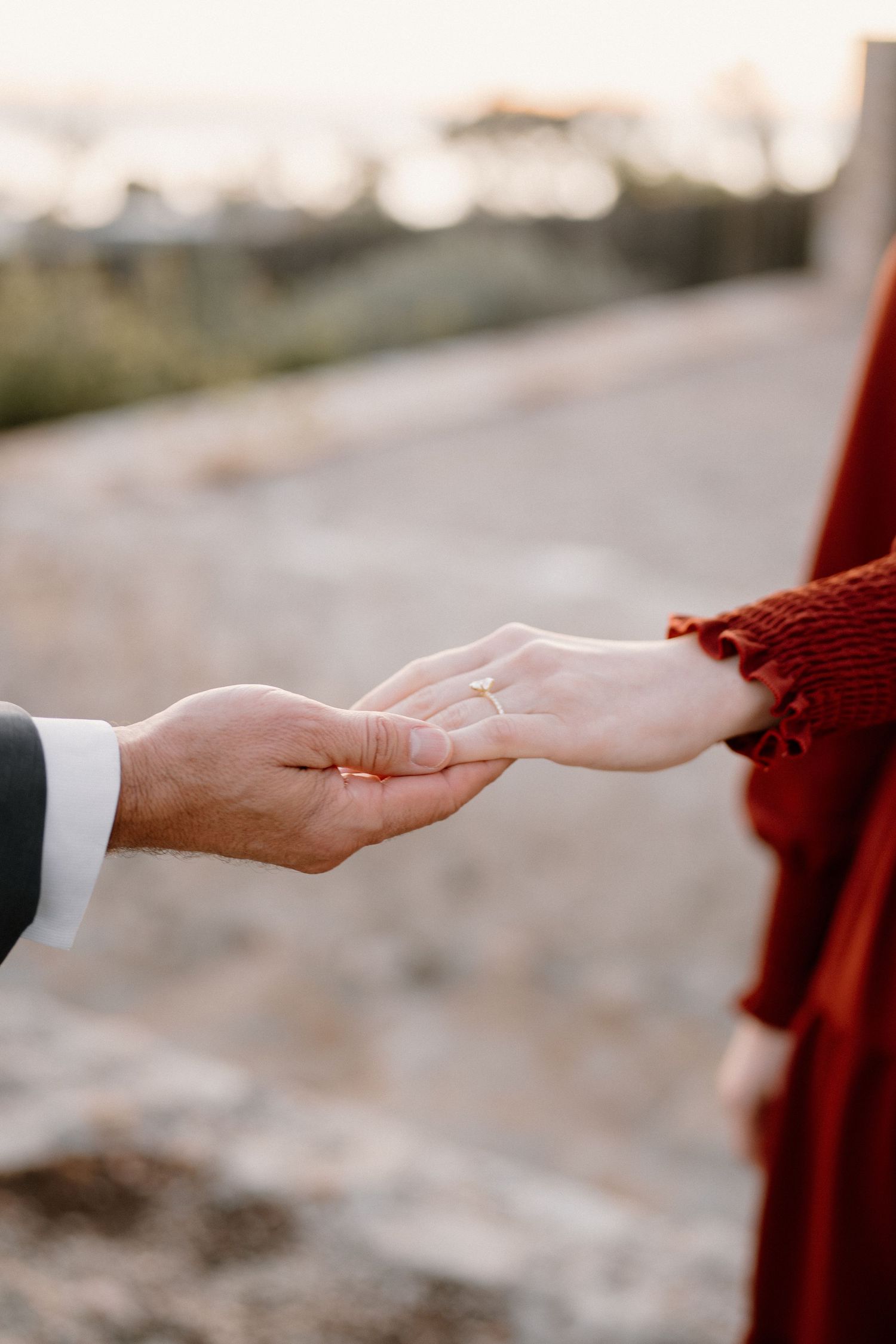 Close-up of an engagement ring on a woman's hand as couple holds hands at sunset.