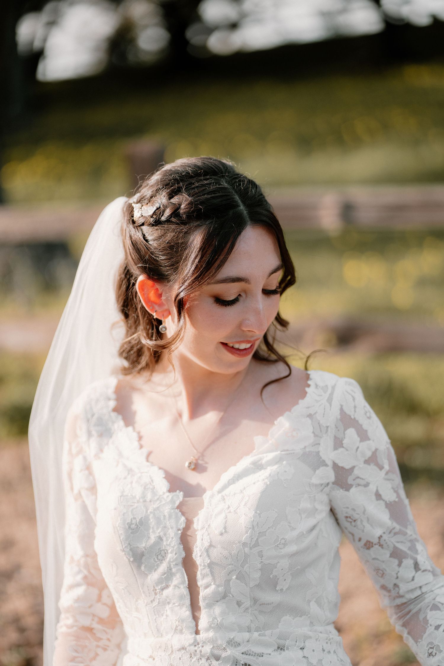 Beautiful bride in long-sleeve lace wedding gown with veil and floral hair accessory in golden light.