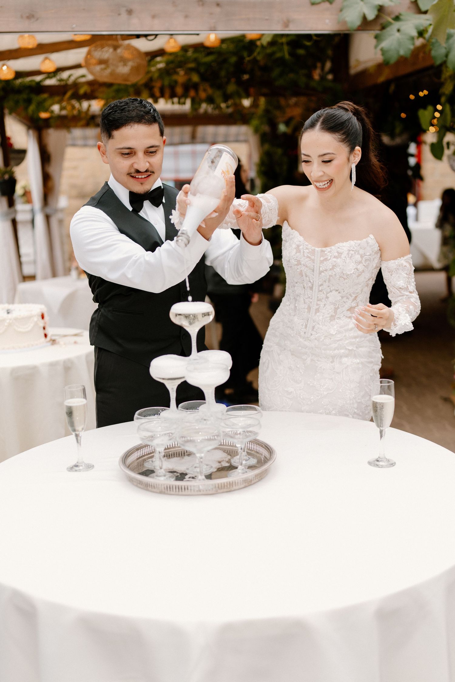 Bride and groom pouring champagne tower at their elegant indoor wedding reception celebration.