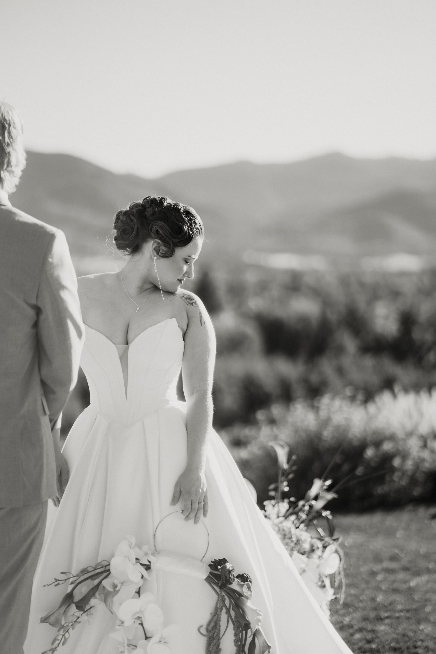 Elegant bride in a strapless ballgown holds a floral bouquet with rolling mountains in the background.