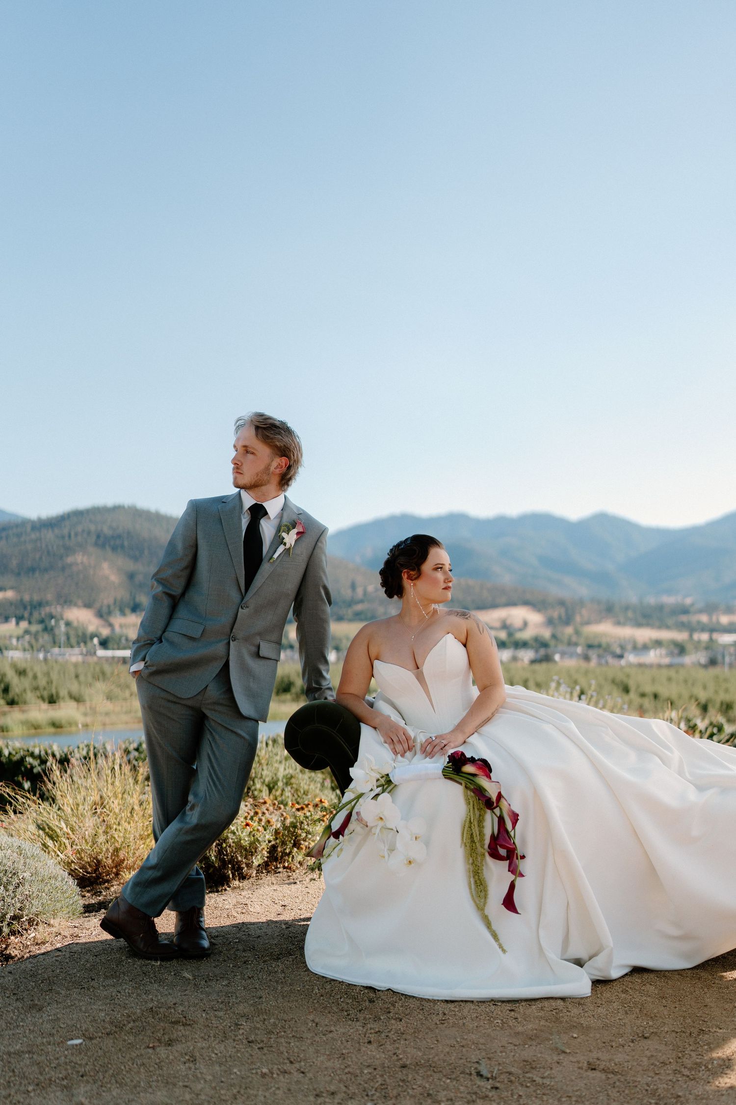 Bride and groom pose with mountain and lake views at their outdoor vineyard wedding in sunny weather.