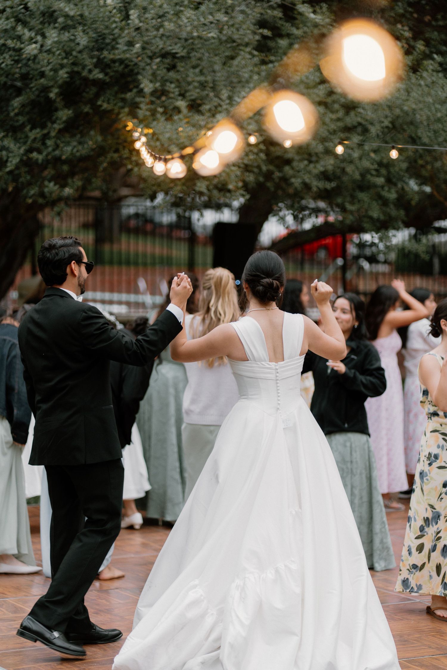 Bride and groom share first dance outdoors under string lights at elegant evening wedding reception.