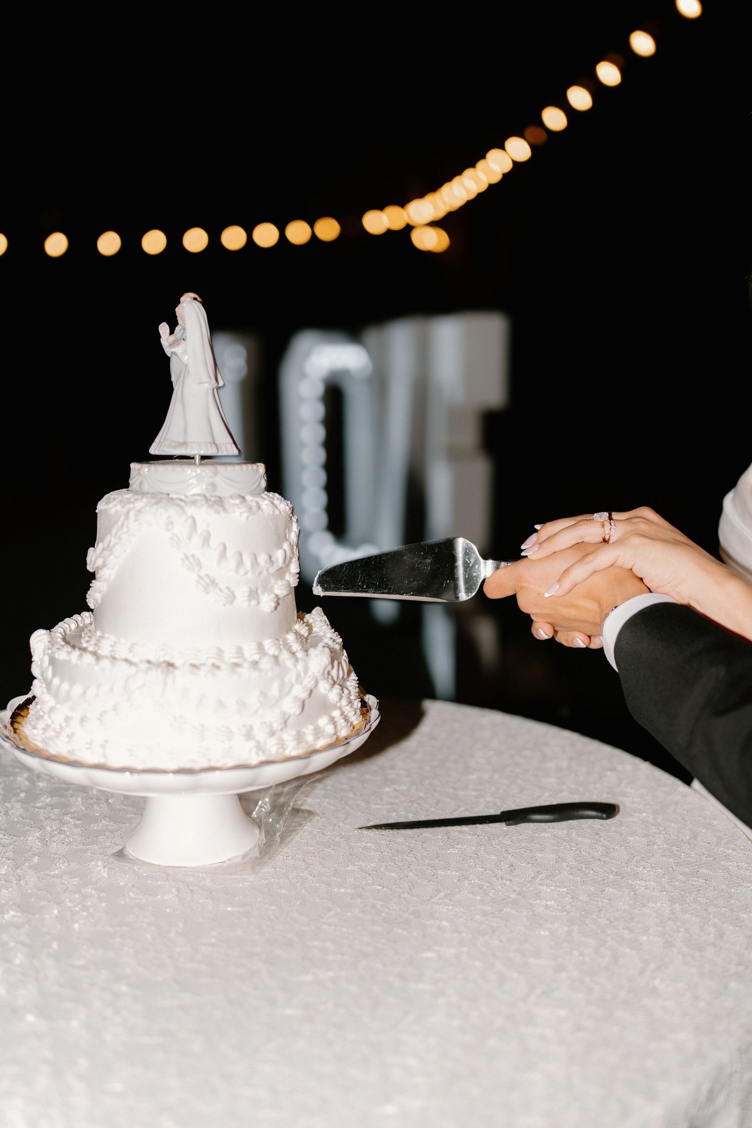 Bride and groom cutting a classic white two-tier wedding cake with figurine topper at reception.