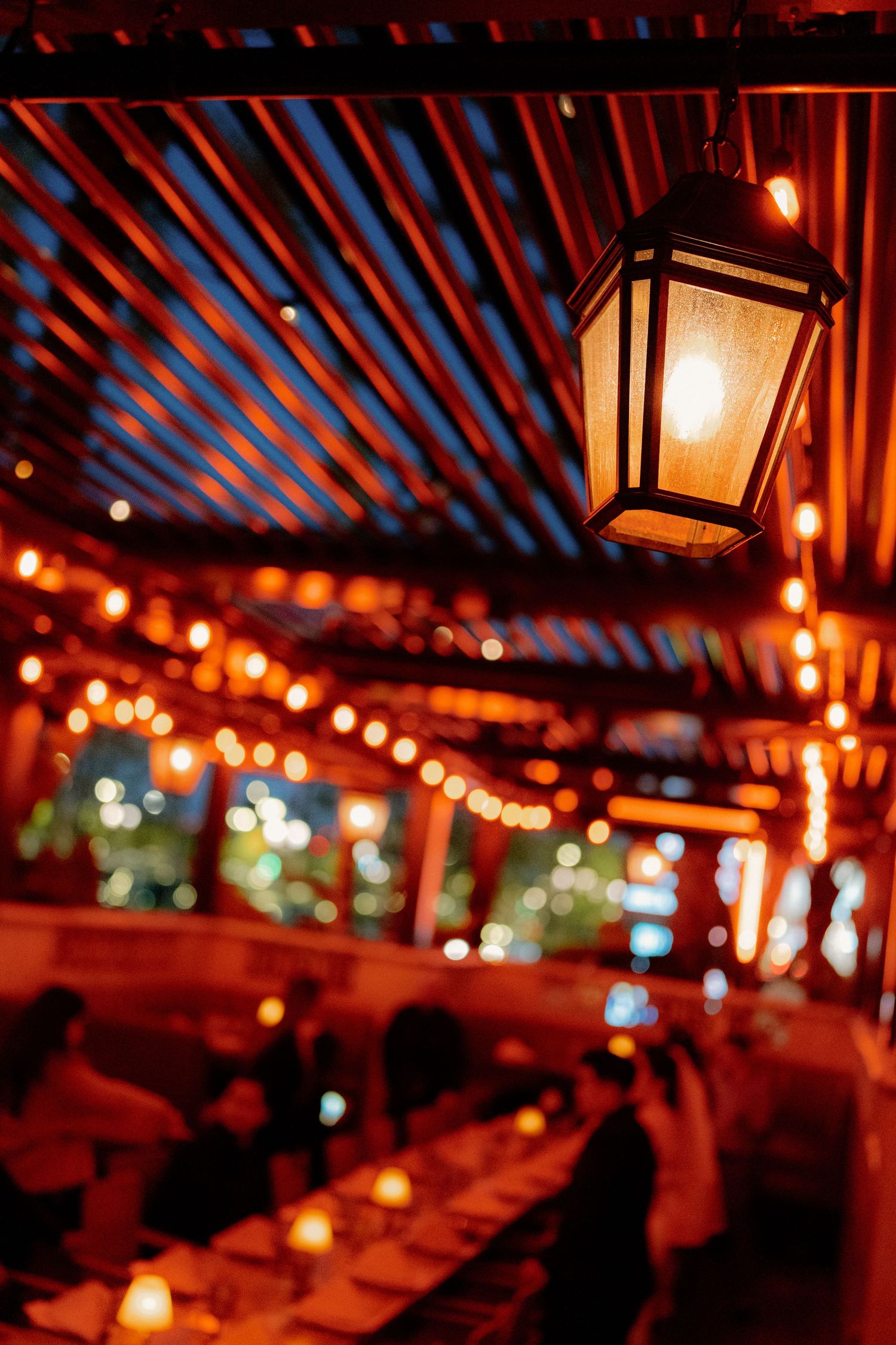 Warm glowing lantern hanging above a dimly lit restaurant interior with string lights and dining guests.