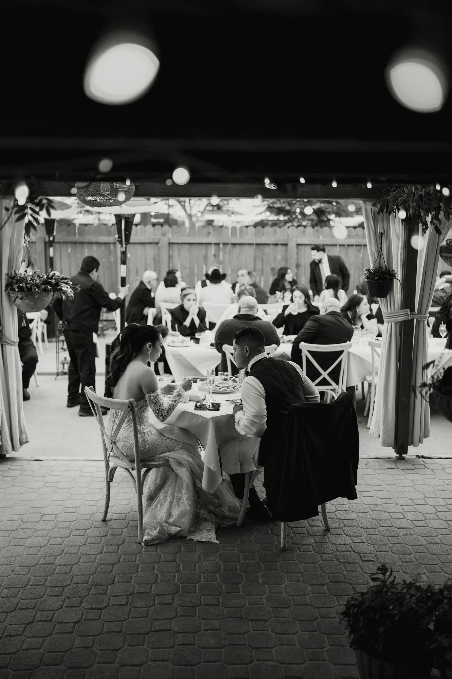 Black and white photo of bride and groom seated at sweetheart table enjoying their wedding reception dinner.