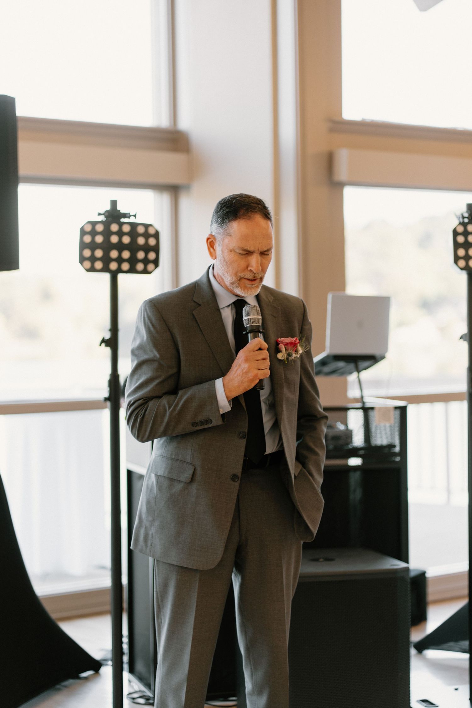 Elegant man in gray suit delivers heartfelt speech at wedding reception while holding a microphone.