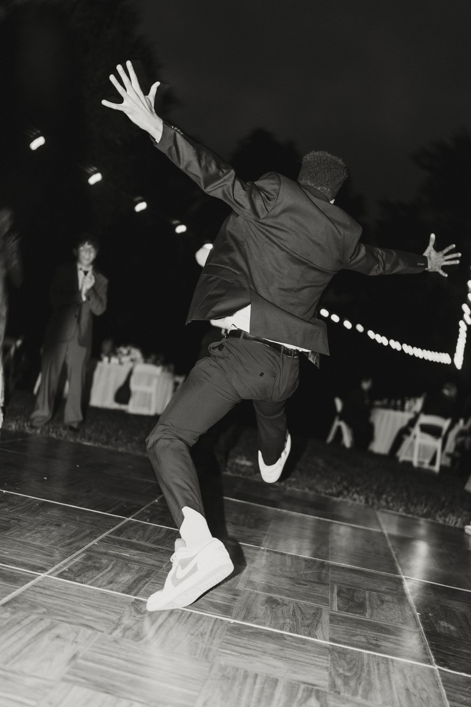 Black and white photo of a guest dancing energetically on outdoor wedding dance floor.