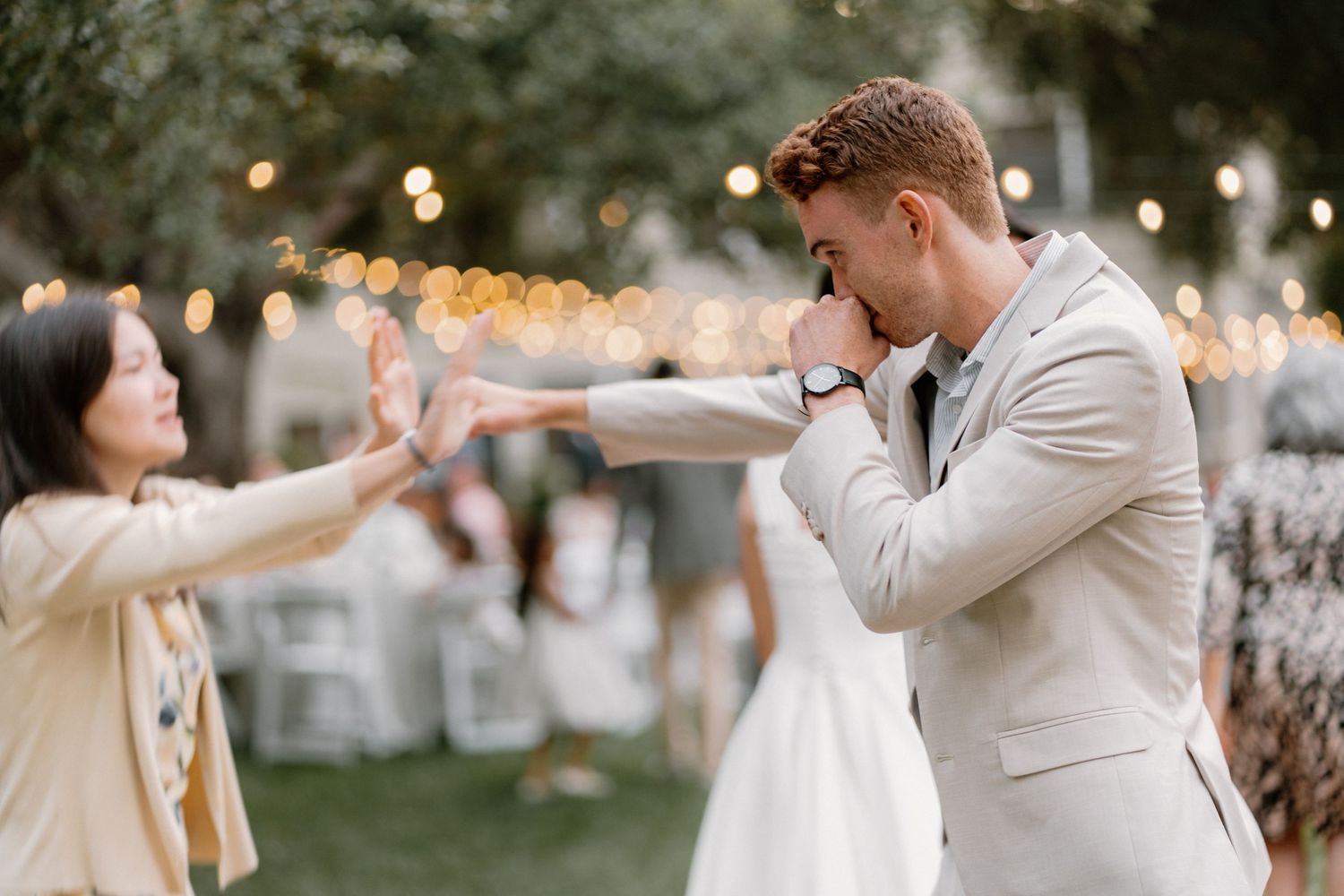 Emotional groom covering his mouth during wedding first look reaction outdoors with string lights.