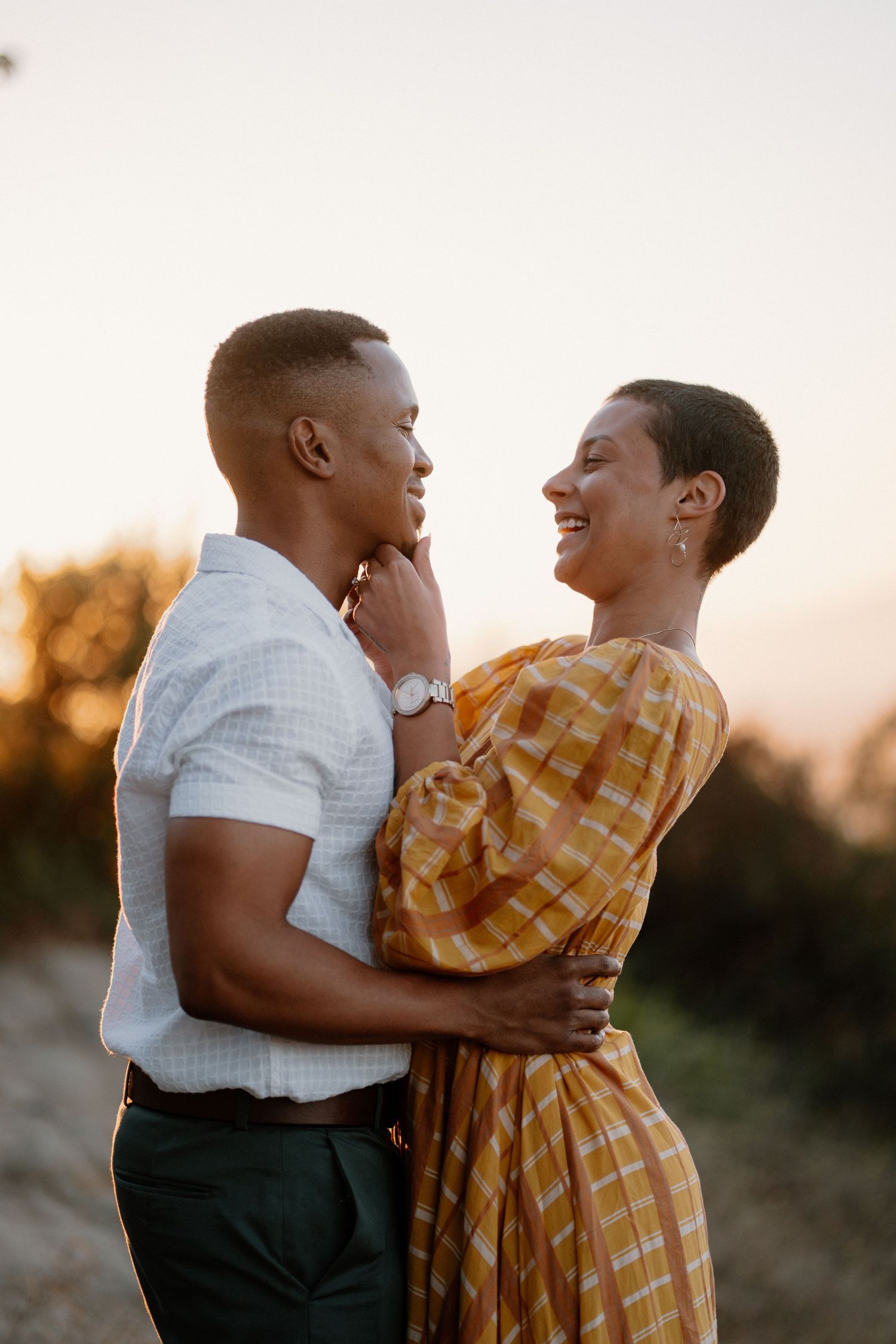 A joyful couple embraces and gazes at each other lovingly during a romantic outdoor sunset photoshoot.