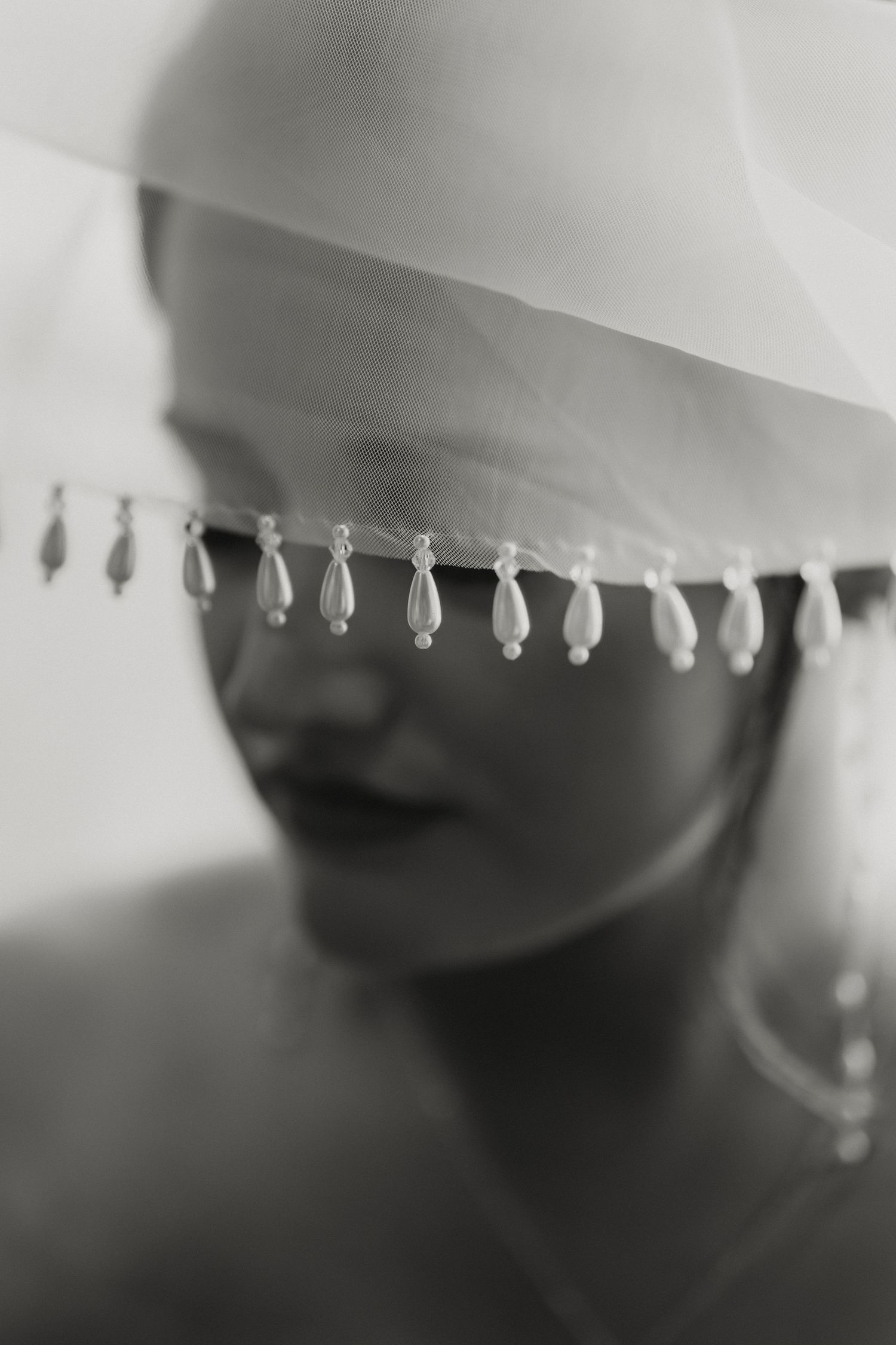 Black and white bridal portrait with pearl-trimmed veil covering eyes.