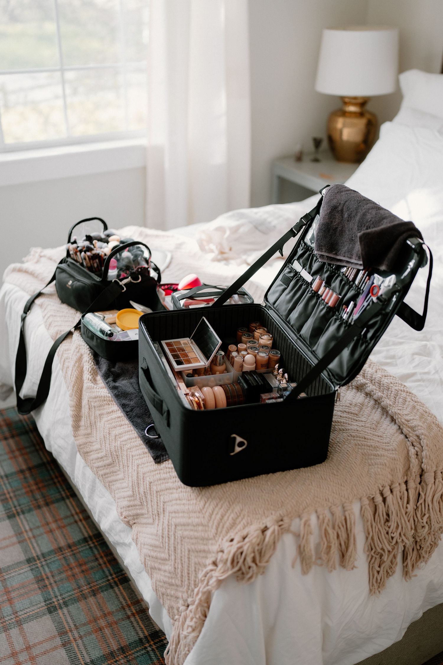 Professional makeup artist kit open on bed displaying organized brushes, palettes, and beauty products.