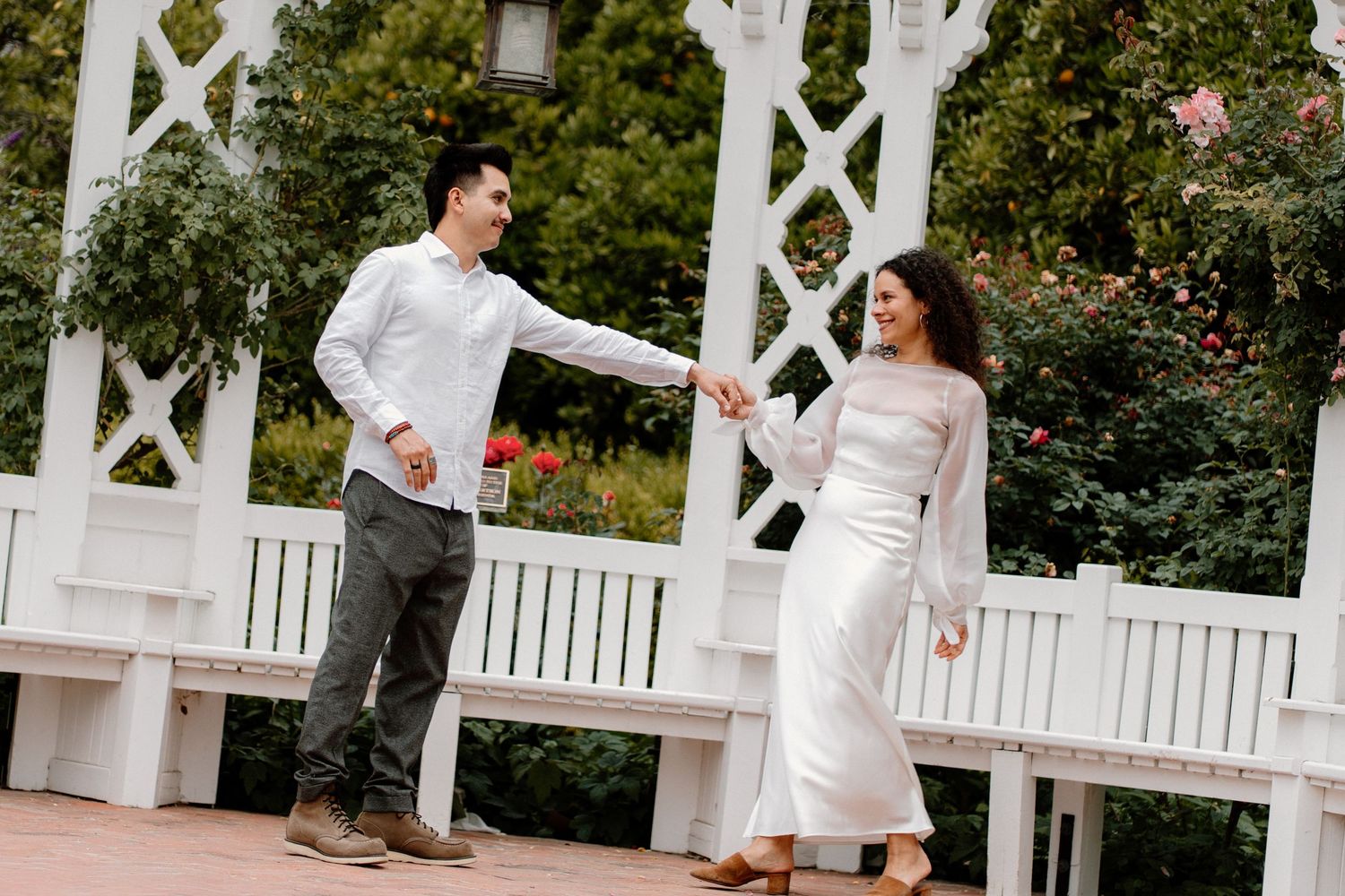 Couple laughing and holding hands while walking on a white pergola deck surrounded by rose gardens.