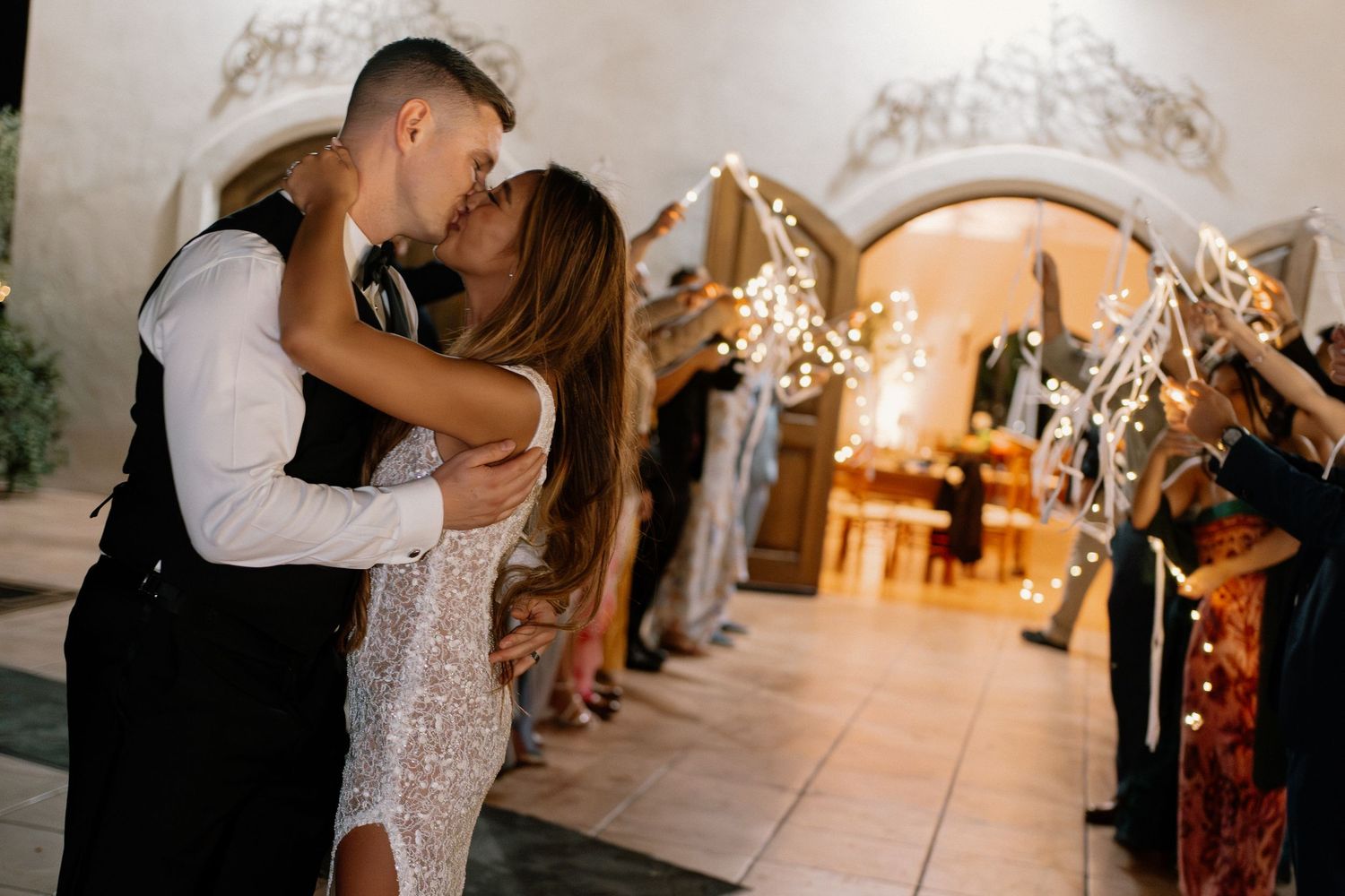 Newlyweds share romantic kiss during sparkler send-off exit at elegant wedding venue.