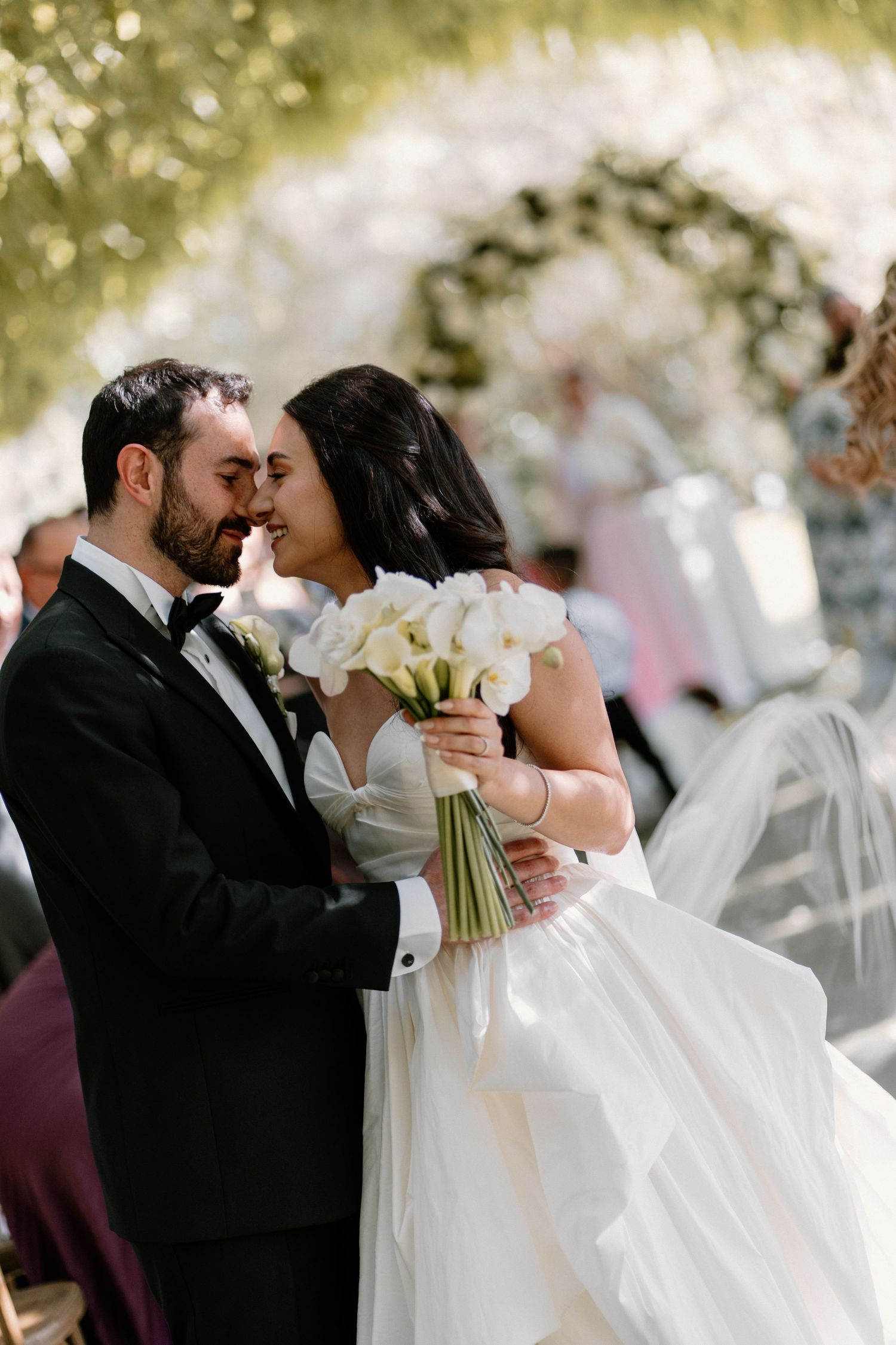 Bride and groom sharing romantic moment at altar with white calla lily bouquet and floral arch.